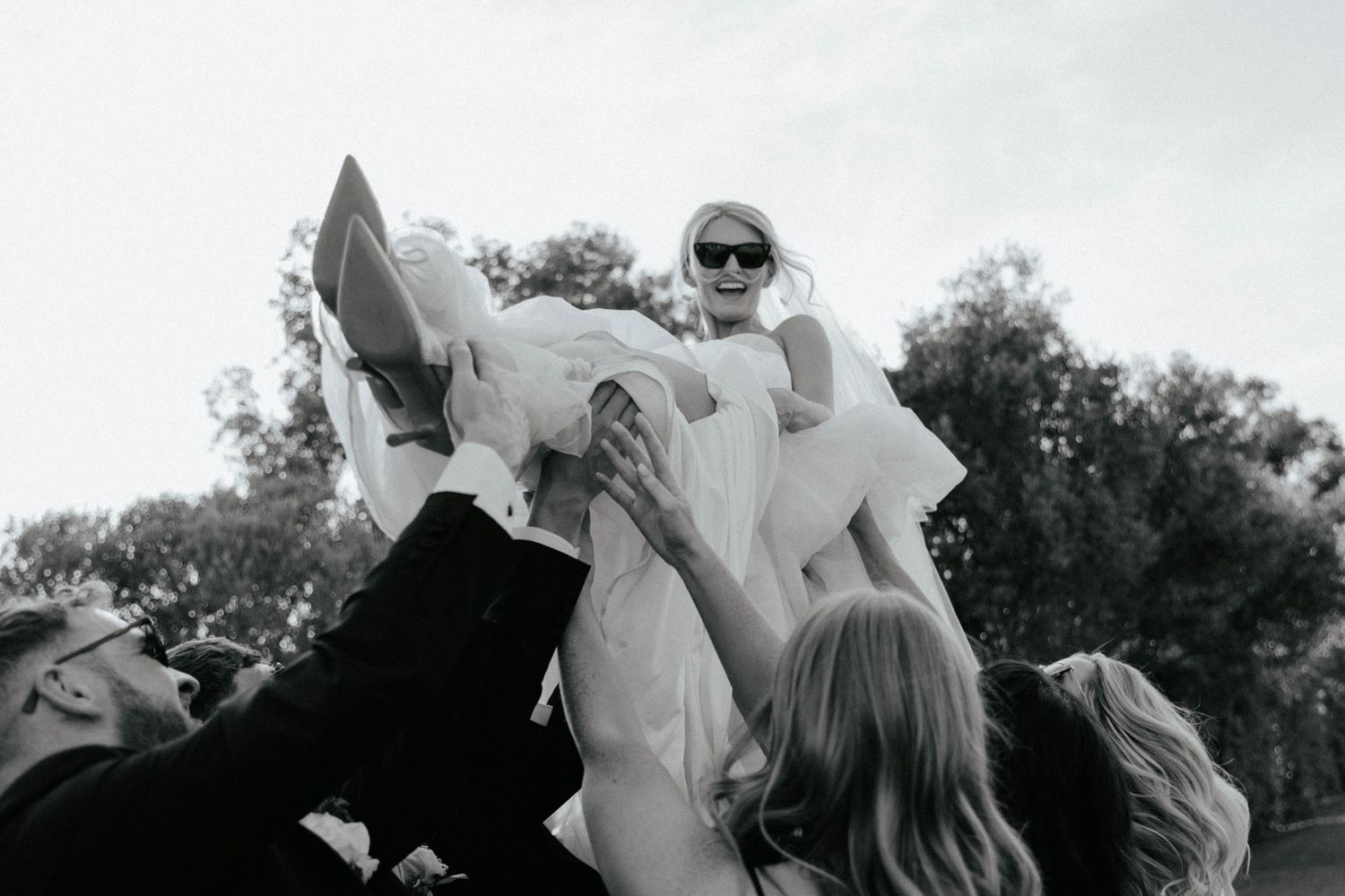 A black and white photograph shows a group of people lifting someone up in celebration outdoors.