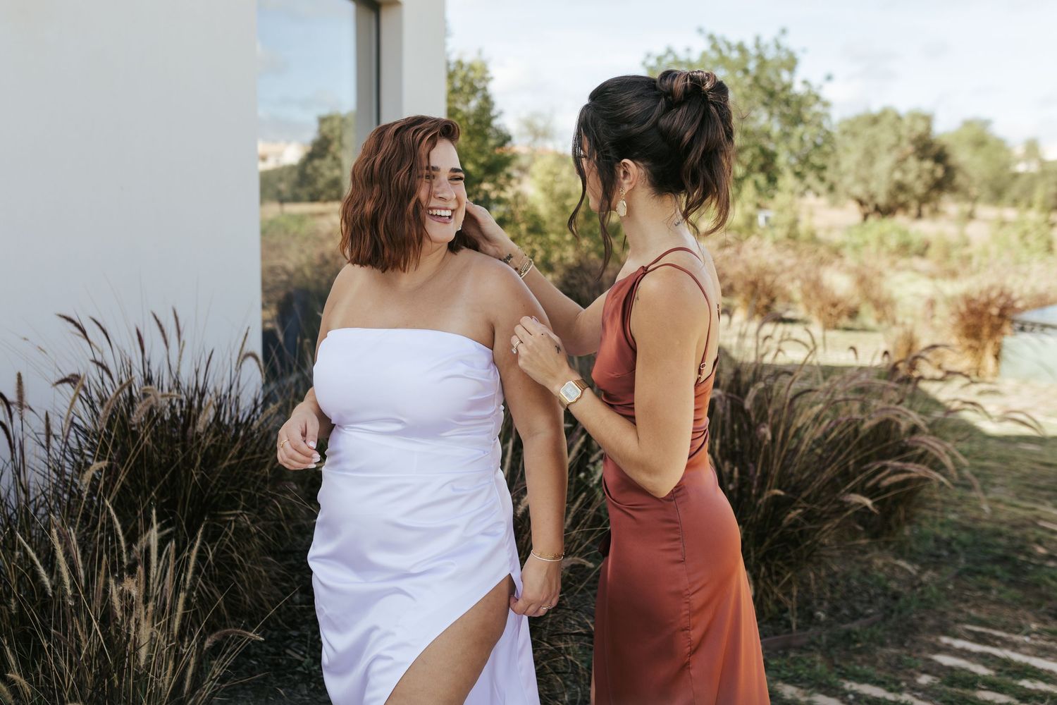 Two women share a joyful moment outdoors with greenery and natural scenery in the background.