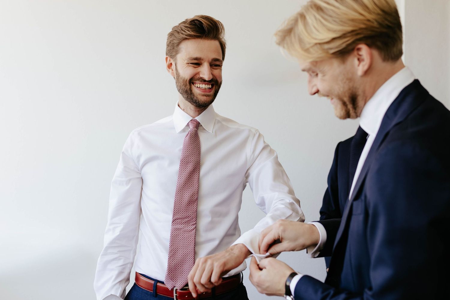 Two businesspeople sharing a light moment as they look at a wristwatch or smartwatch together against a white wall.