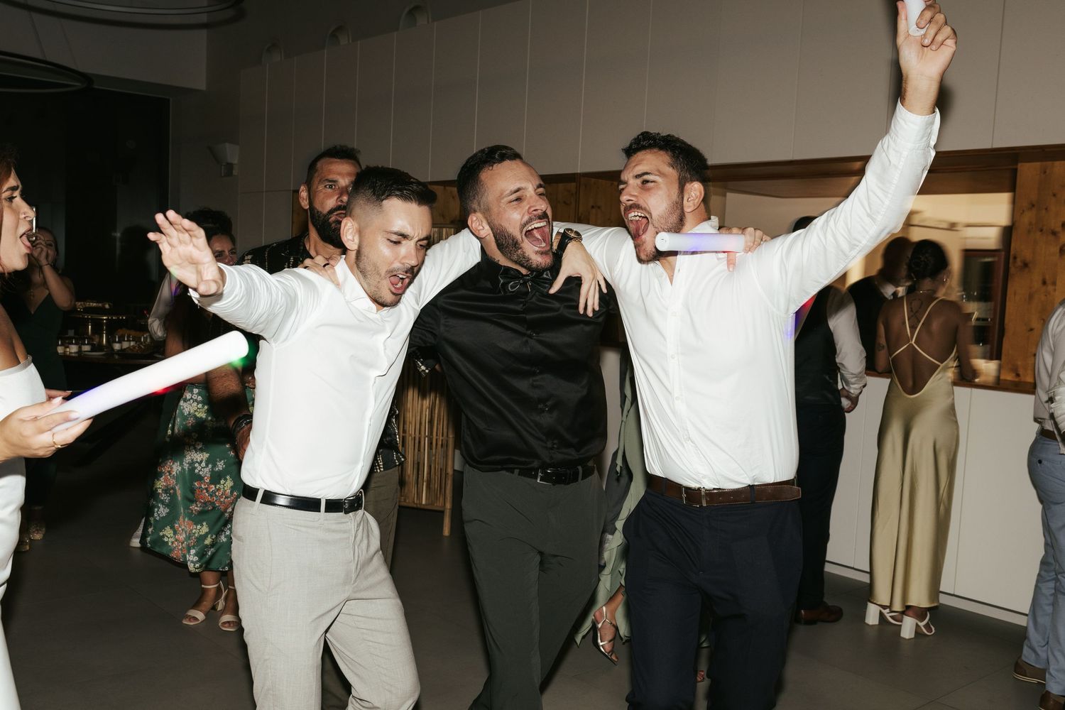 Group of people in white dress shirts and dress clothes dancing and celebrating with raised arms at a party.