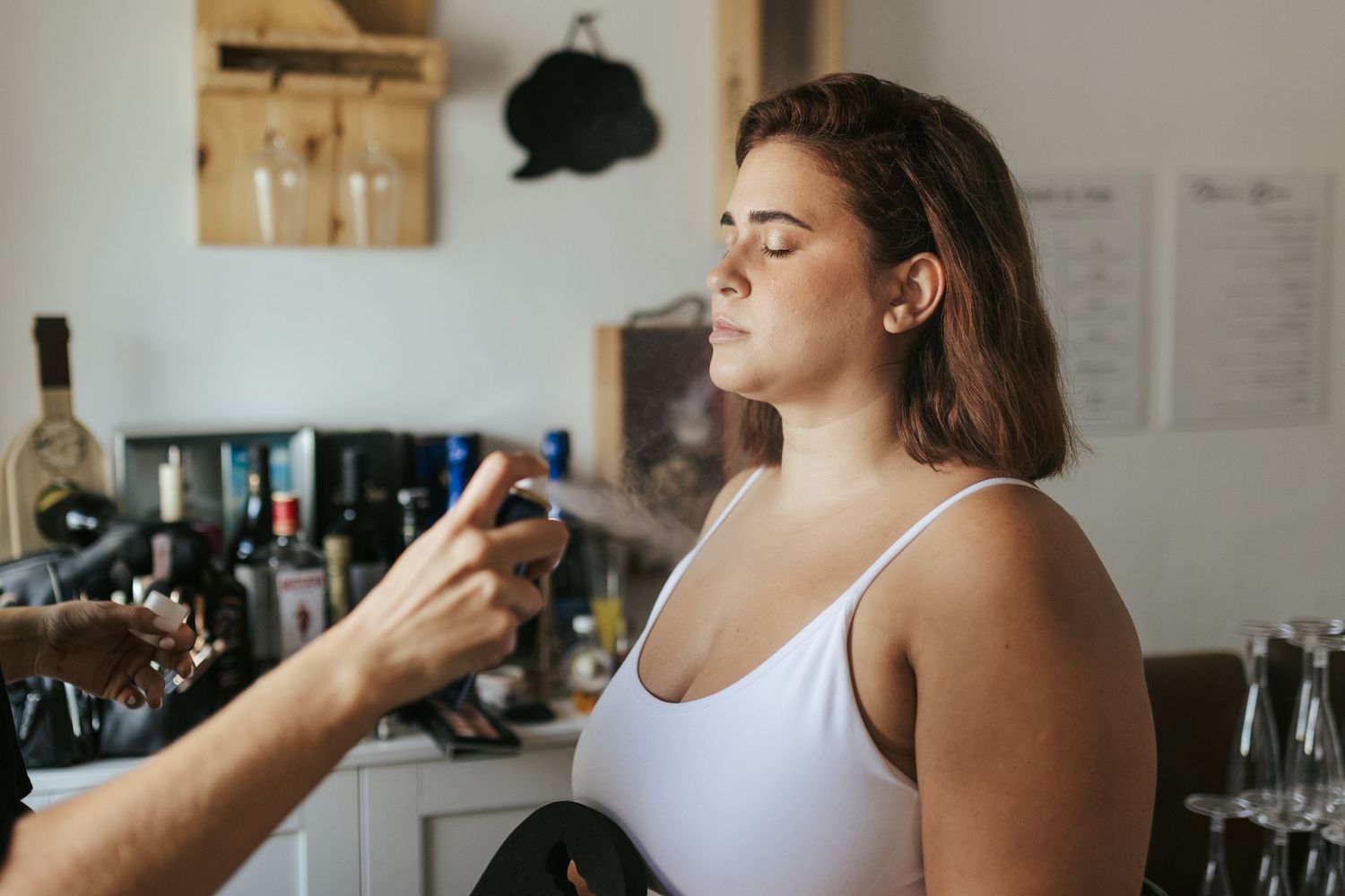 A person in a white tank top stands at a bar counter while someone sprays a mist over their drink.