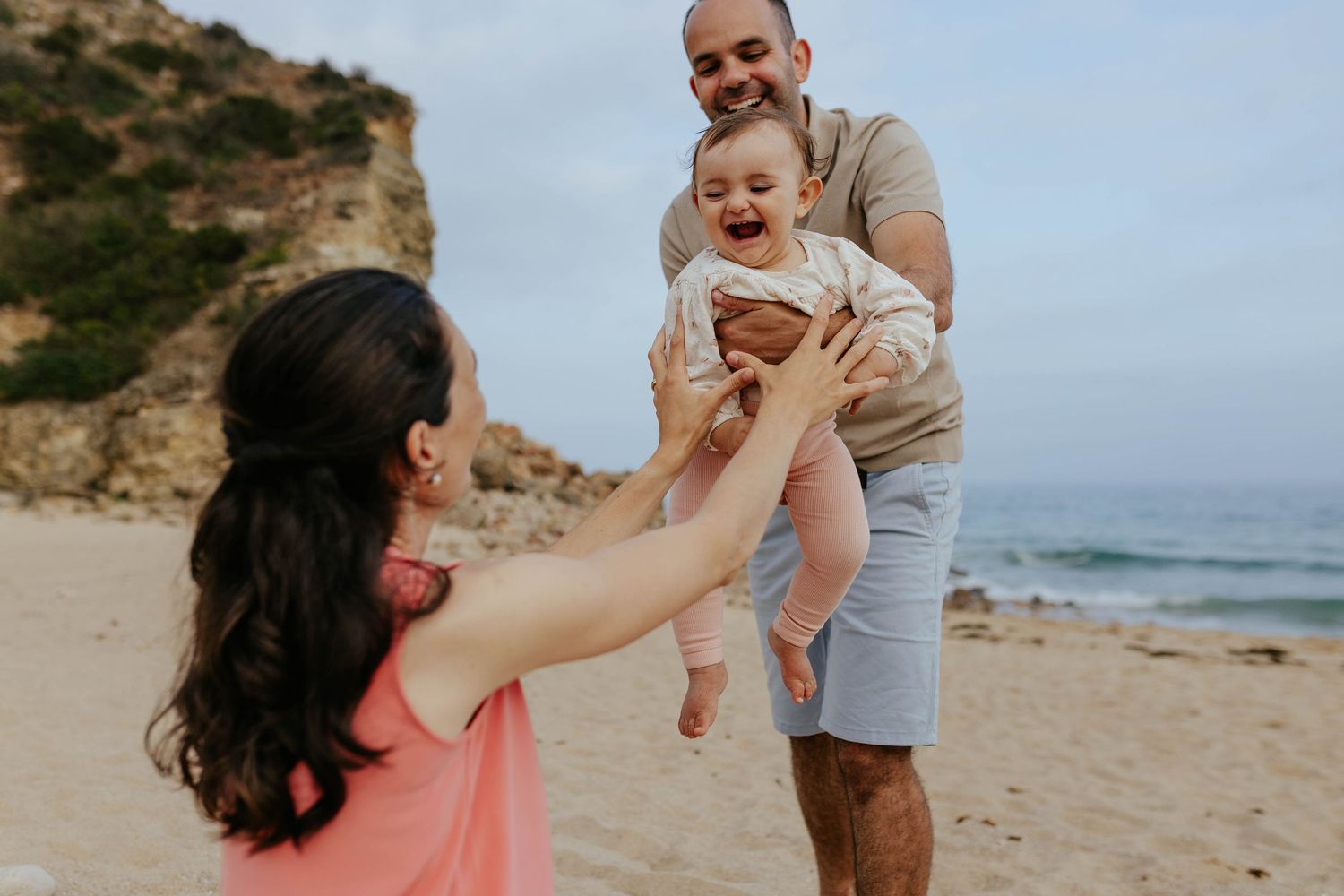 A family shares a joyful moment together while playing on a scenic beach with coastal cliffs in the background.