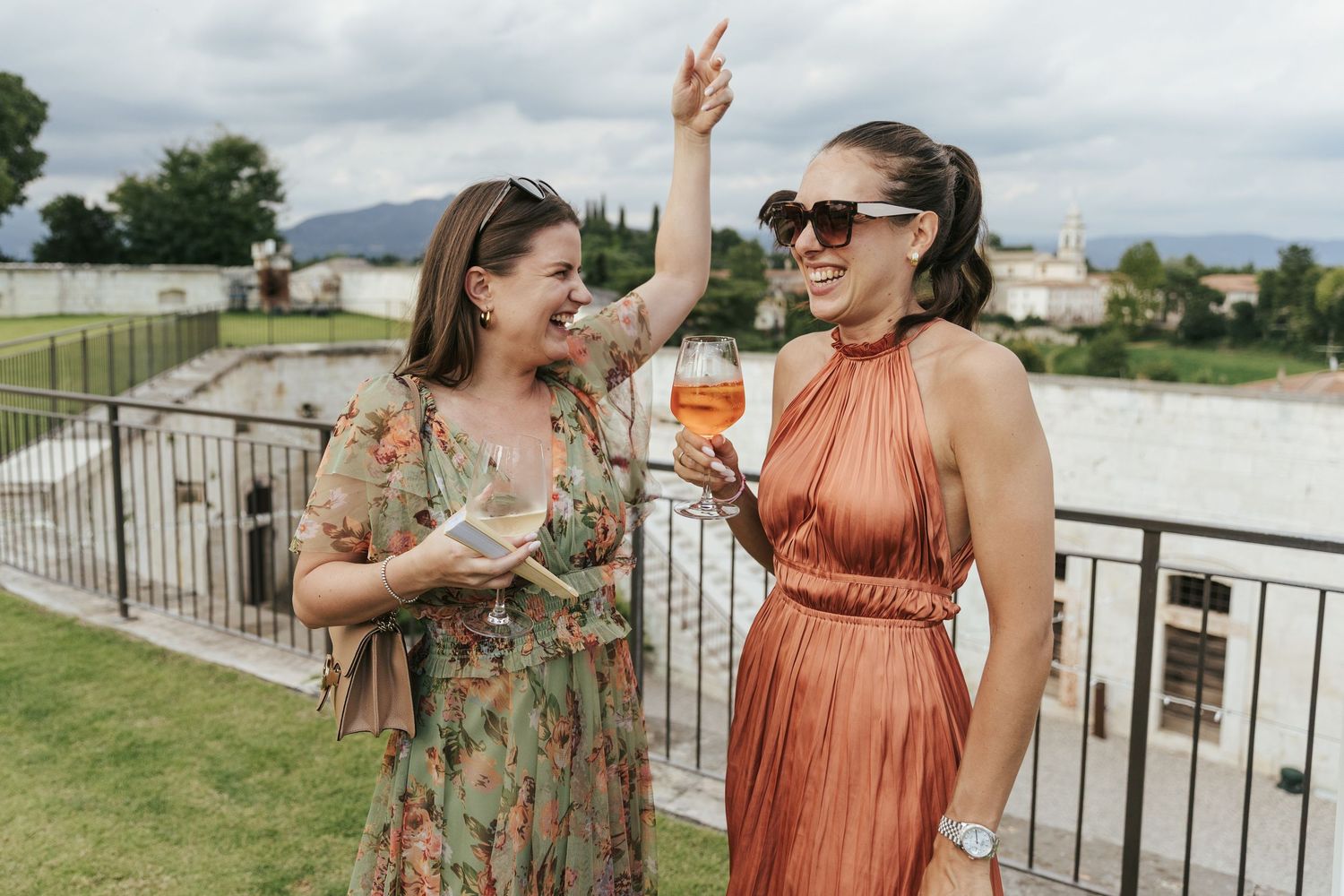 Wedding guests in colorful dresses share laughs during an outdoor celebration.