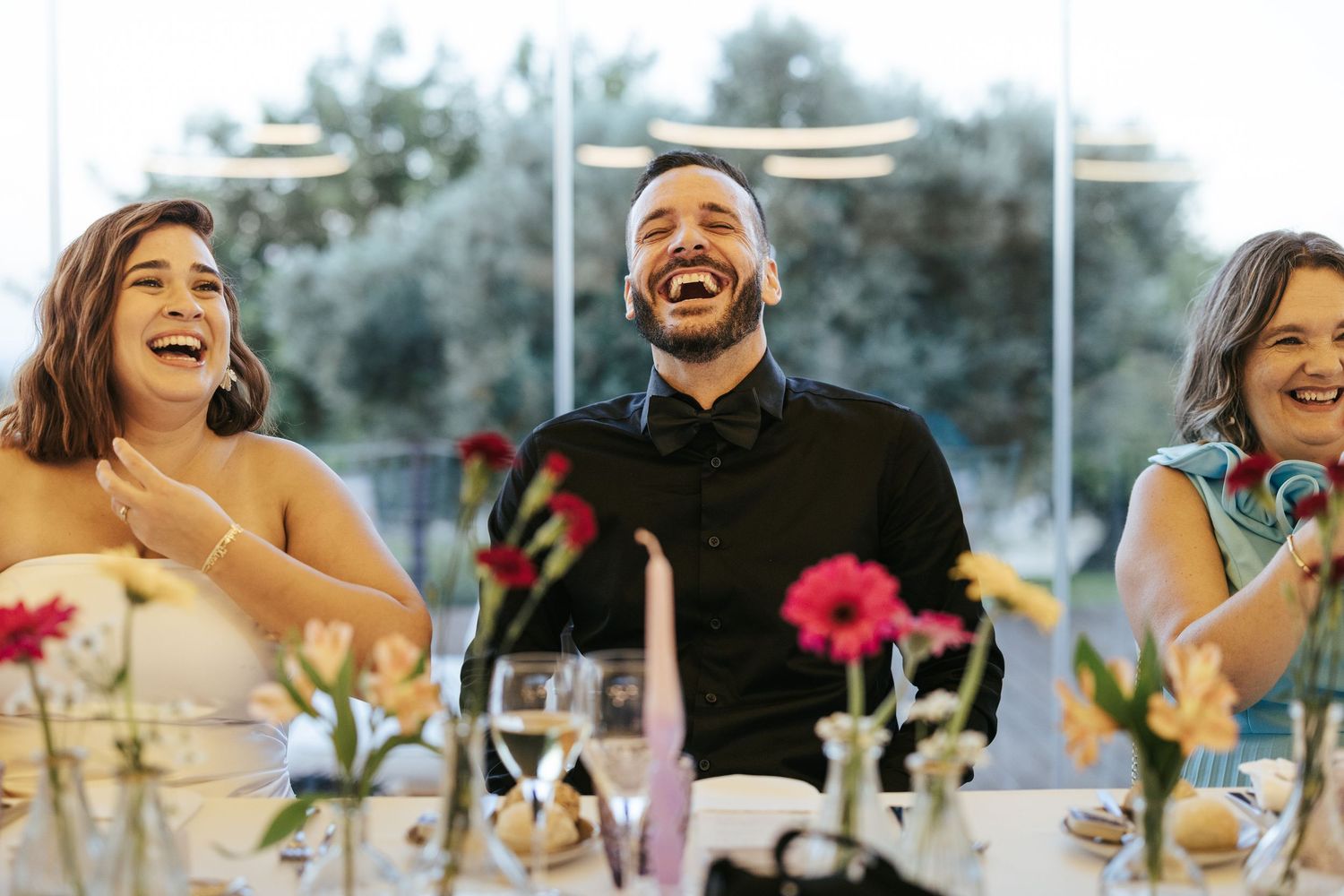People laugh together at a wedding reception table decorated with colorful flower centerpieces.