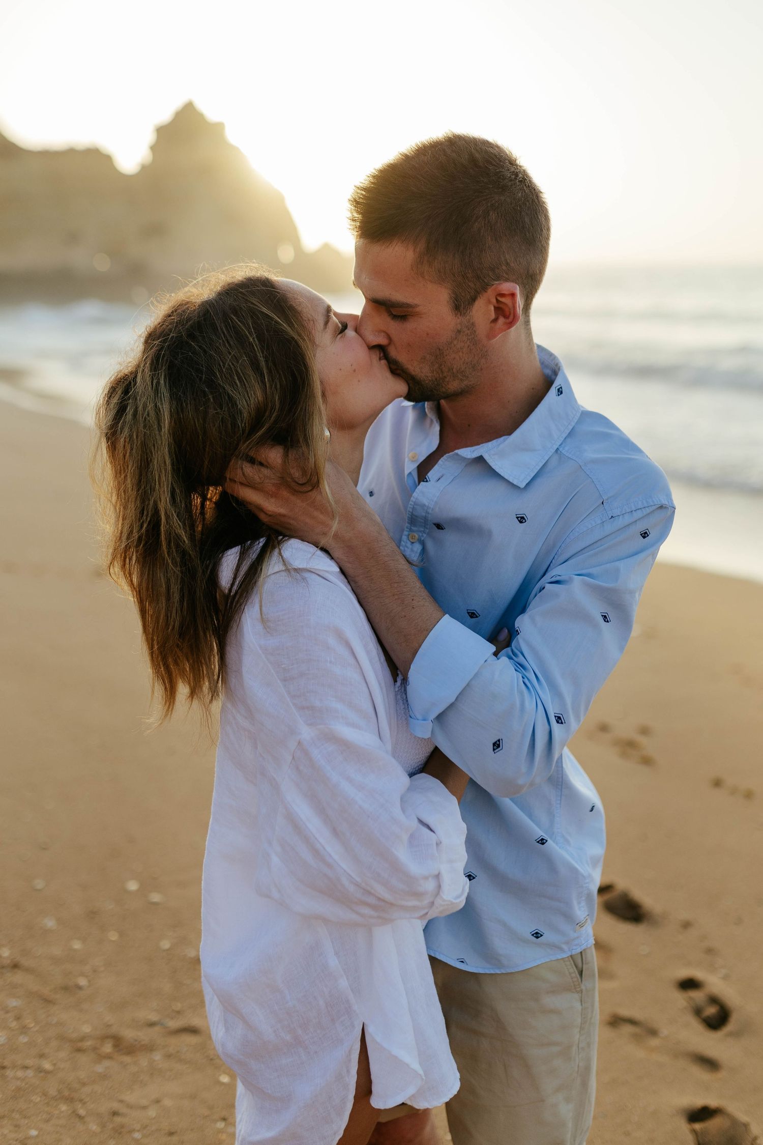 A passionate kiss shared between a couple on a beach with coastal cliffs at sunrise. Praia Dona Ana, Lagos, Algarve, Portugal.