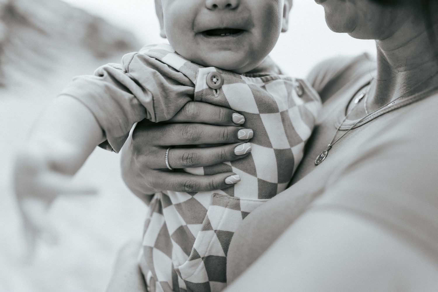 Close-up black and white photo of adult hands holding an infant wearing a geometric patterned onesie.