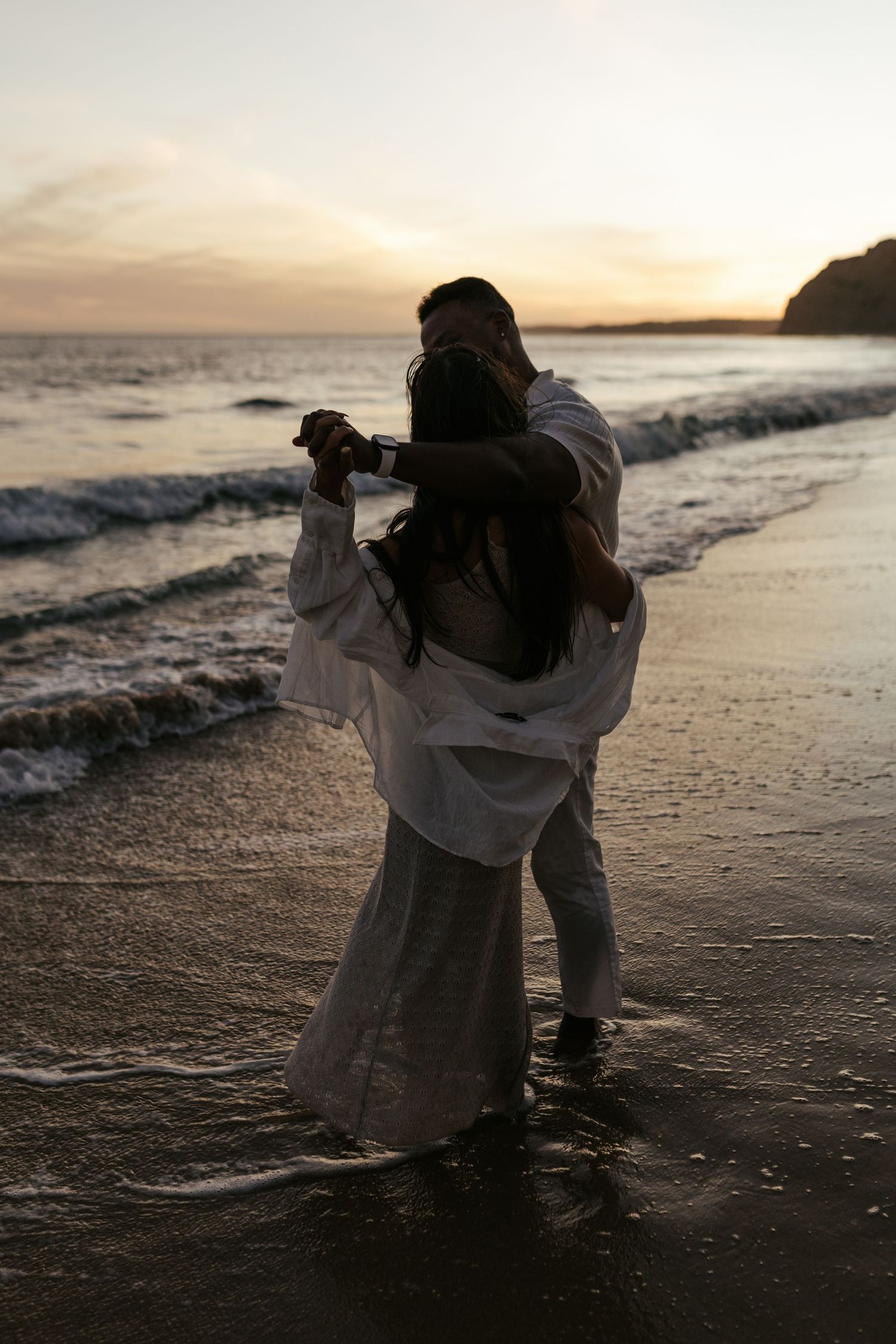 A silhouetted couple dances romantically on the beach during sunset. Praia do Porto de Mós, Lagos, Algarve, Portugal.