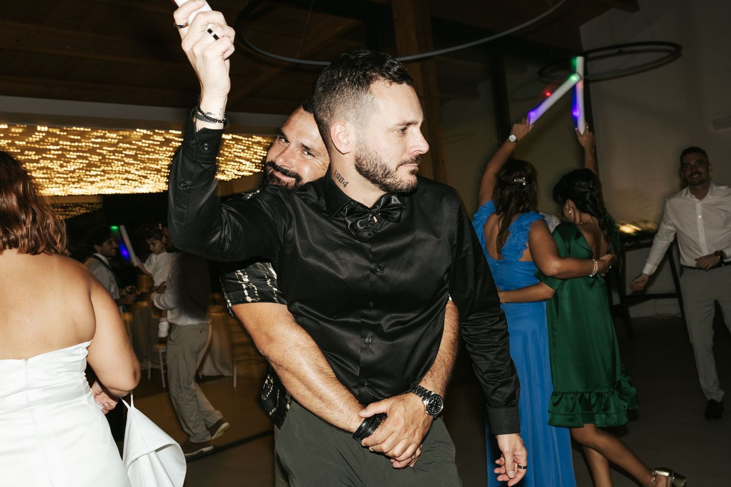 Guests dancing energetically on a reception dance floor under decorative lighting.