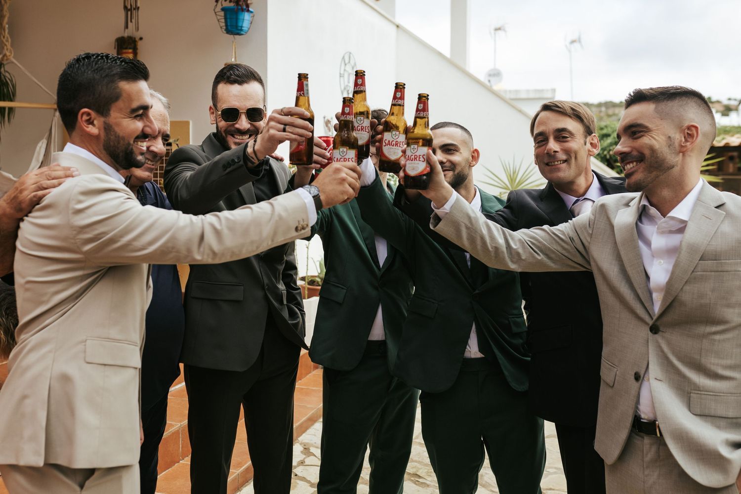 A group of well-dressed companions raise beer bottles in celebration while smiling and laughing together.