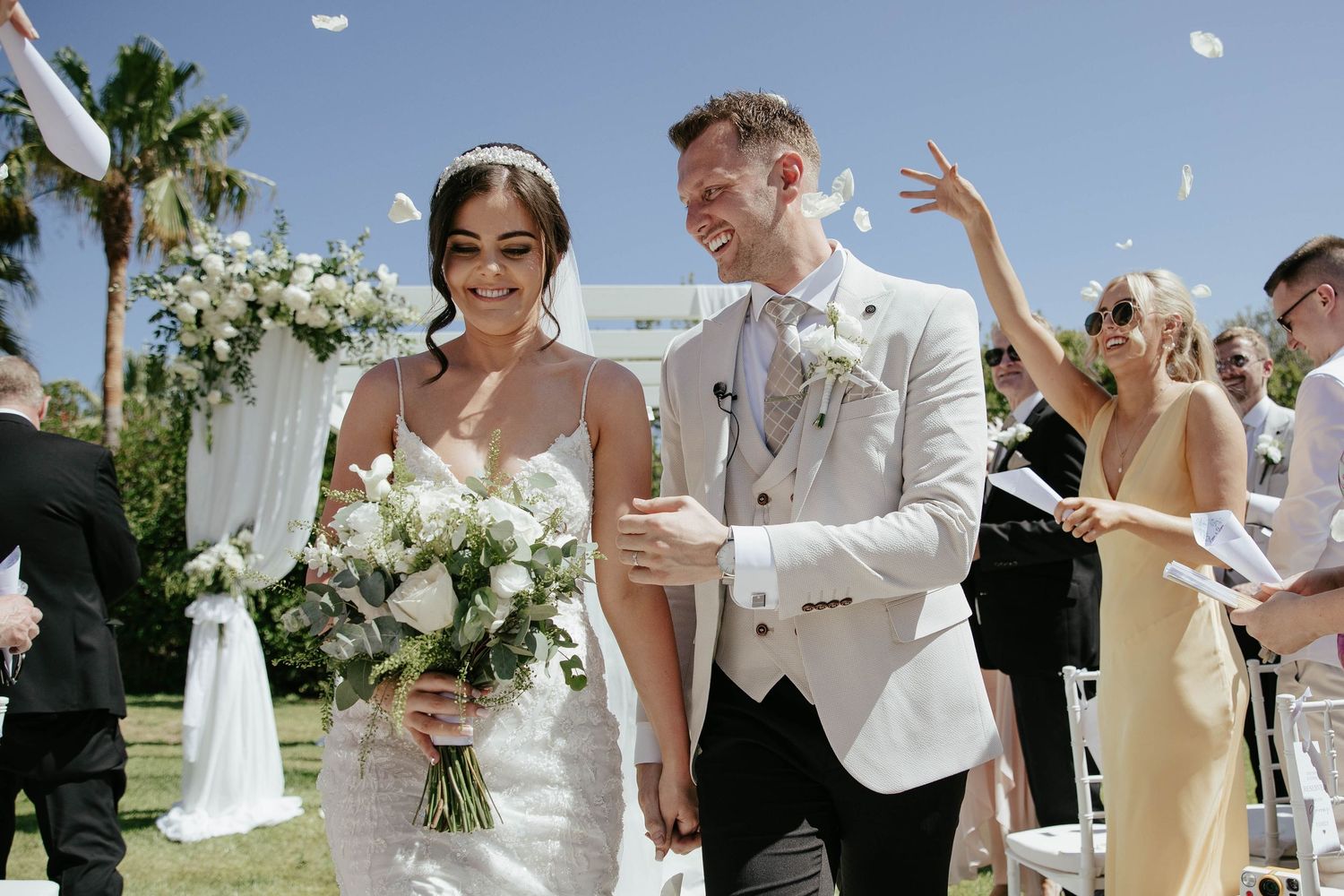A joyful wedding ceremony outdoors with rice confetti falling as the newlyweds walk down a grassy aisle.