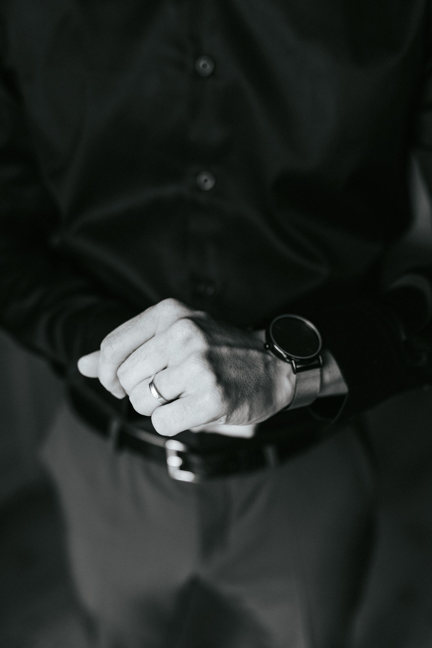 Monochrome image of hands clasped together with a dark wristwatch and button-up shirt.