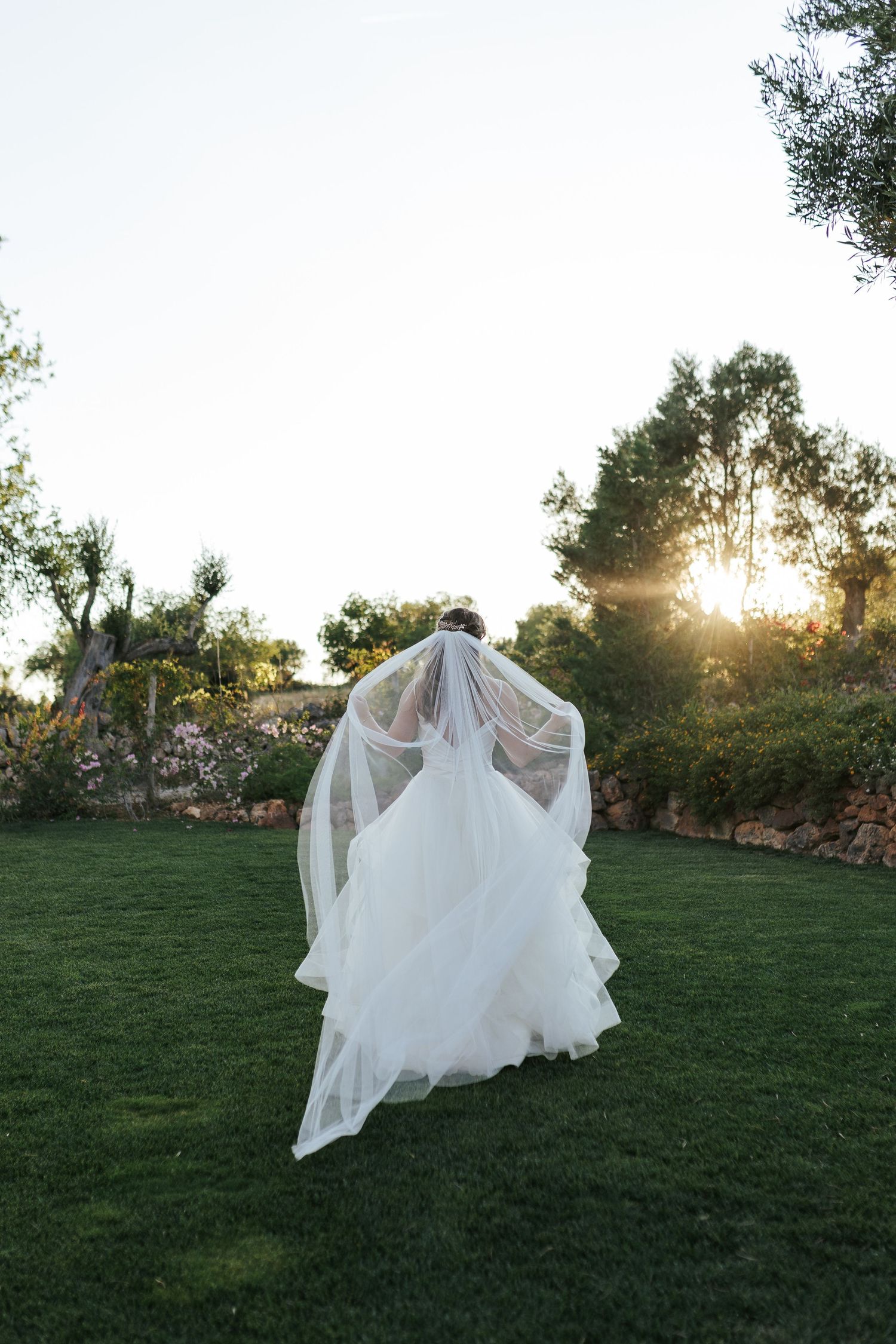 Flowing white wedding dress and veil floating in a dreamy garden setting with sunset peeking through trees. Monte do Serrinho, Algarve.