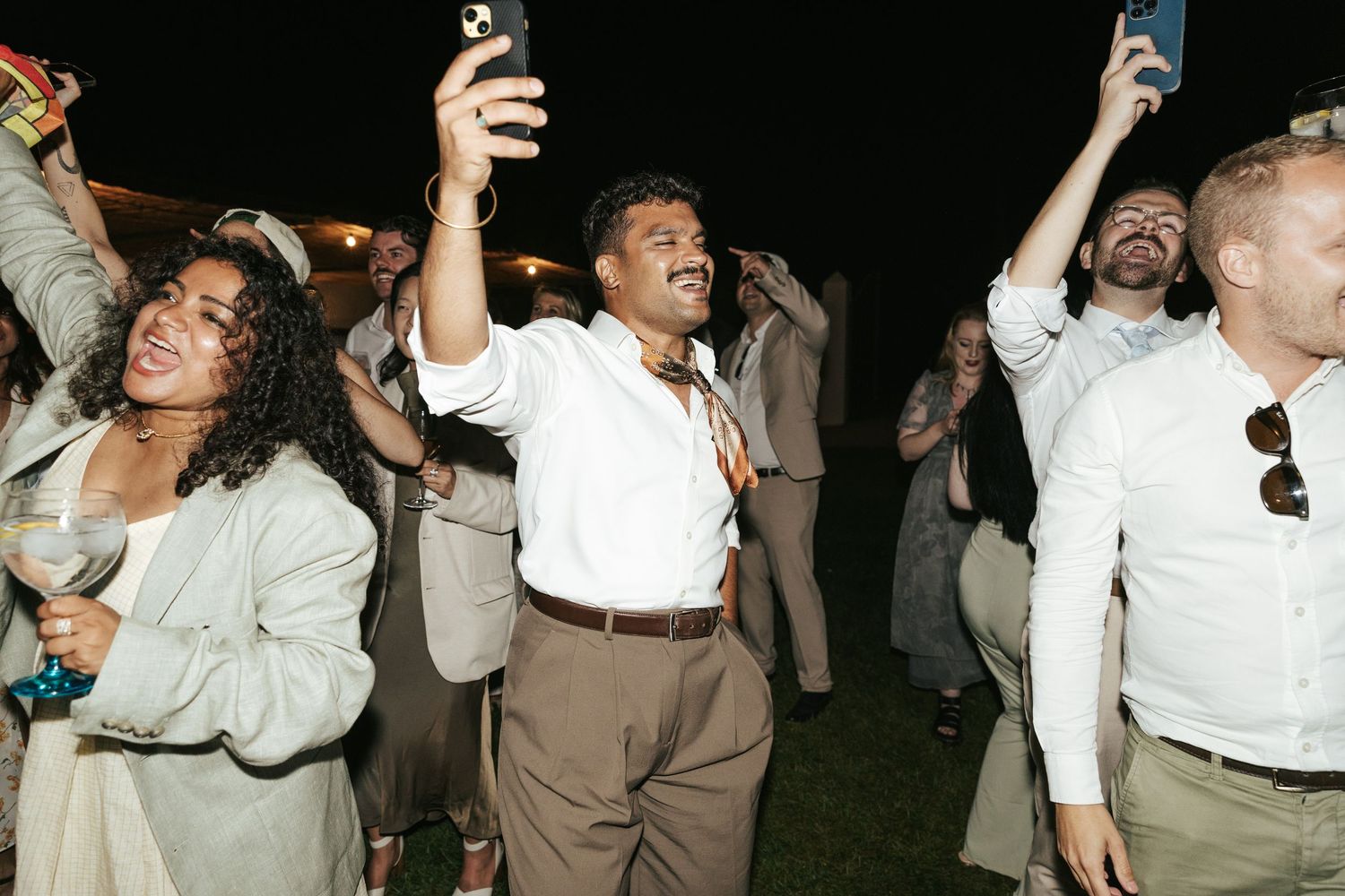 Guests dancing and taking selfies at a lively outdoor evening wedding reception.