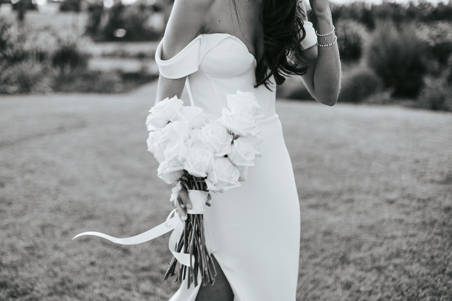 A bride in an elegant white wedding dress holds a bouquet while standing outdoors in a garden setting.
