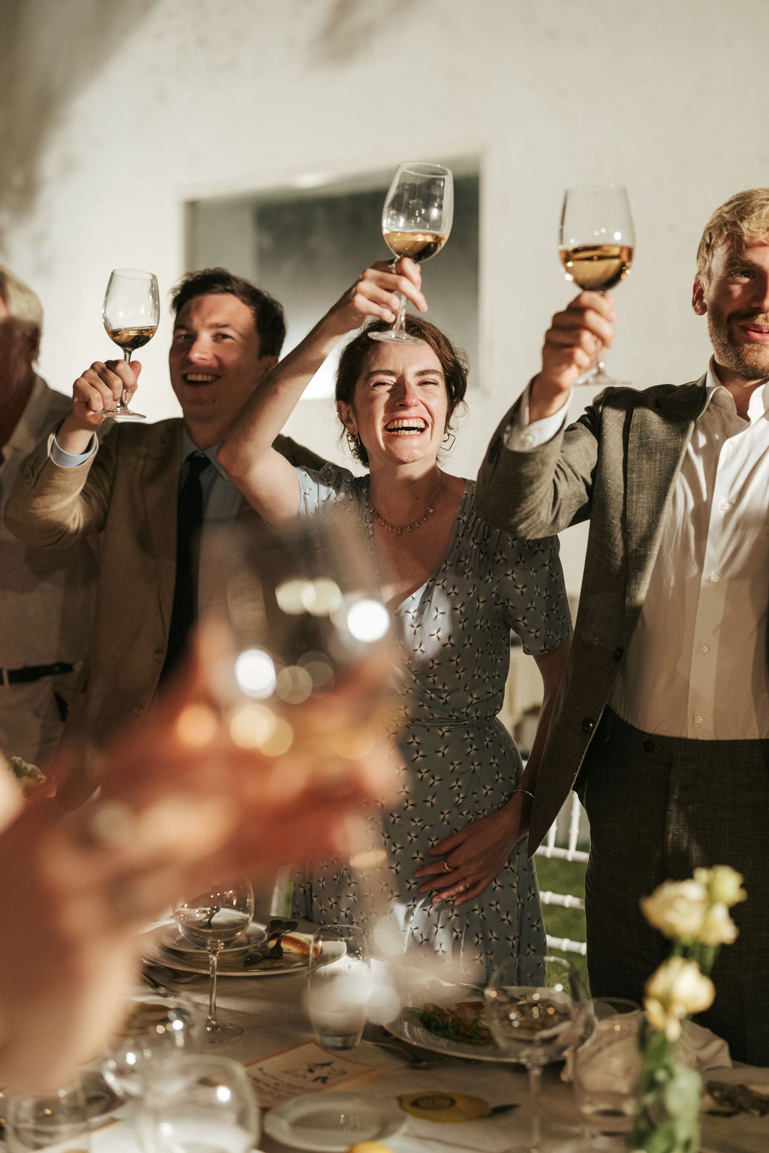 Joyful guests raising wine glasses in a toast at an indoor wedding reception celebration.