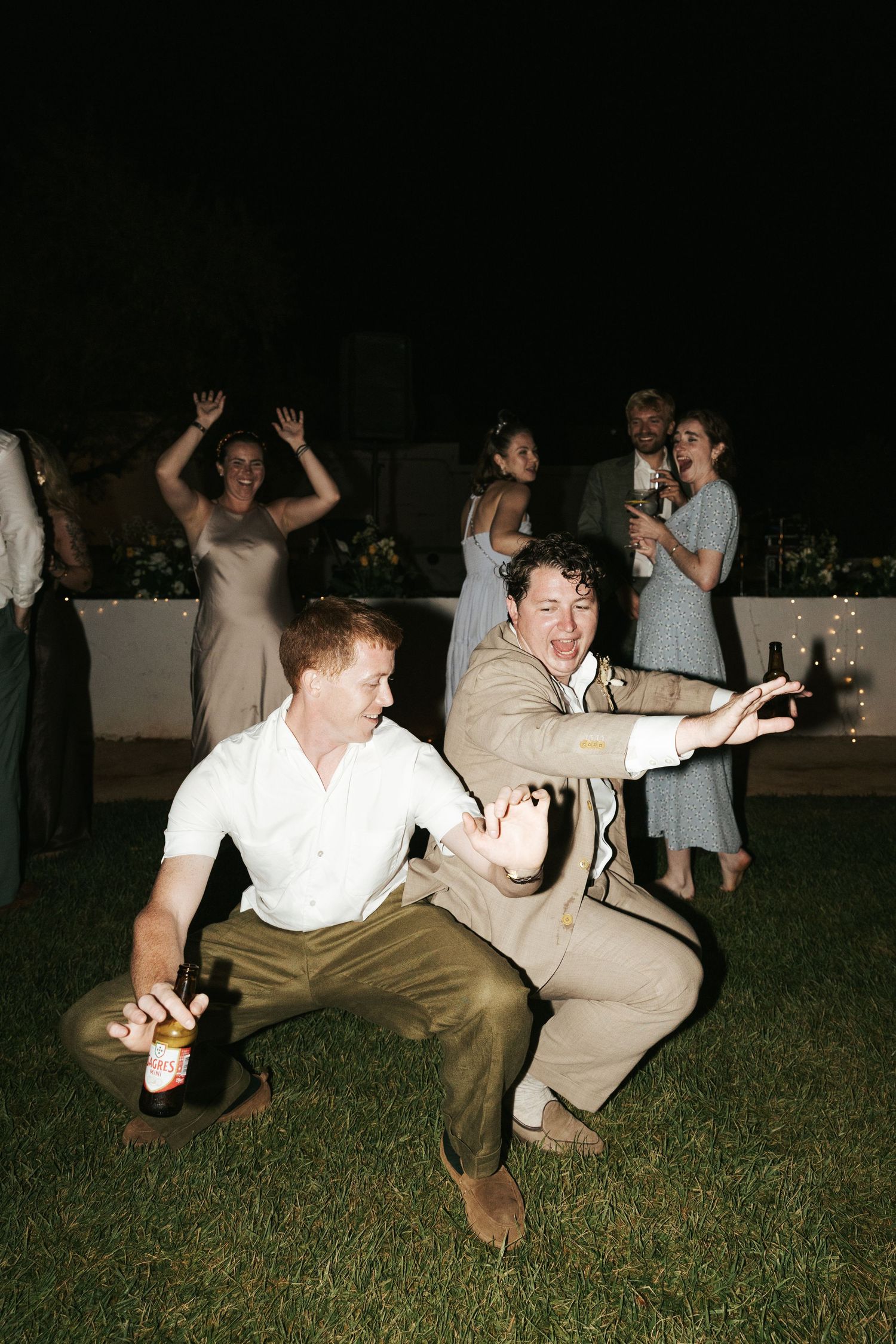 Two men doing playful dance moves at an outdoor nighttime wedding reception party.