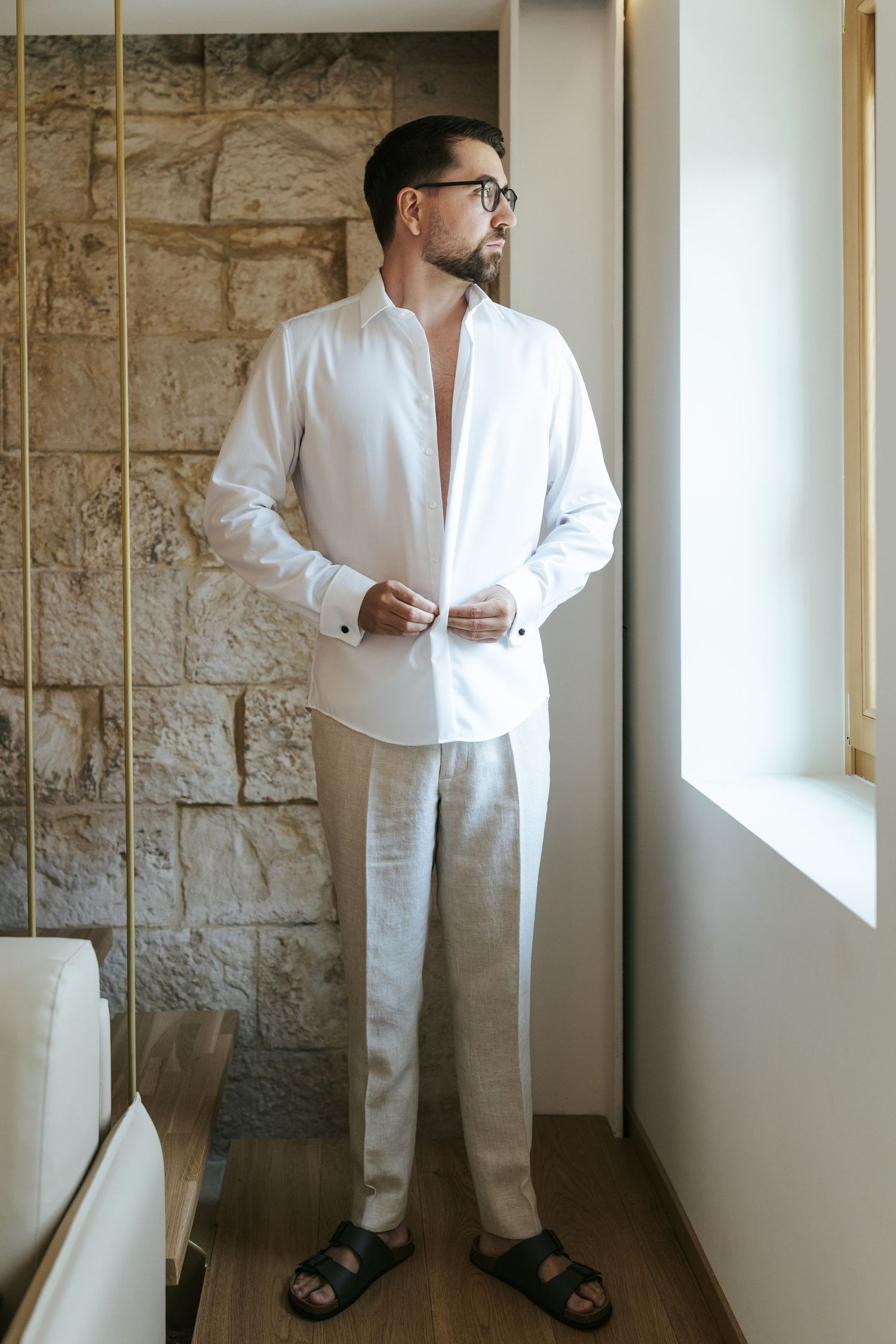 Person wearing all white attire standing against a textured stone wall.