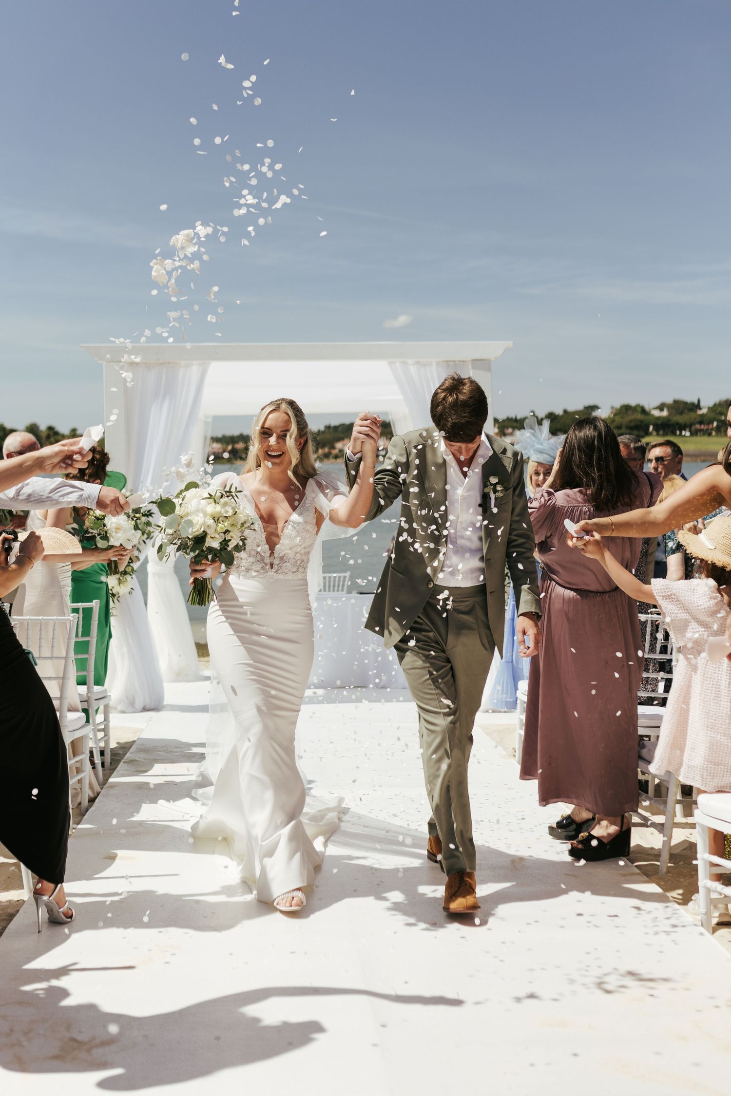 Newlywed couple walks down aisle while guests shower them with confetti at outdoor beach wedding ceremony. Casa do Lago, Portugal.
