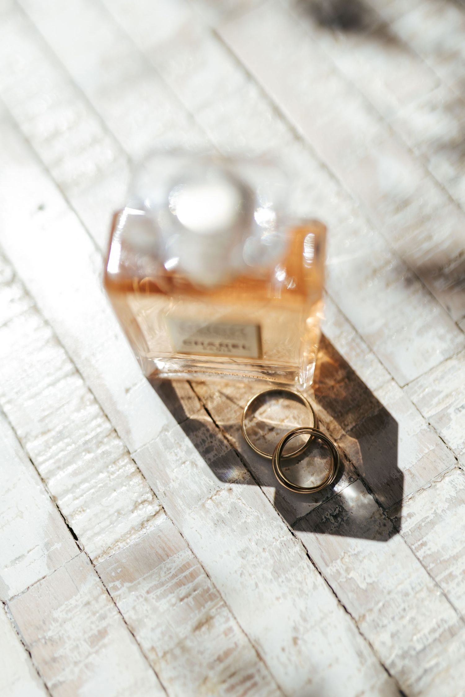 Wedding rings and perfume bottle casting dramatic shadows on a white wooden surface in elegant composition.