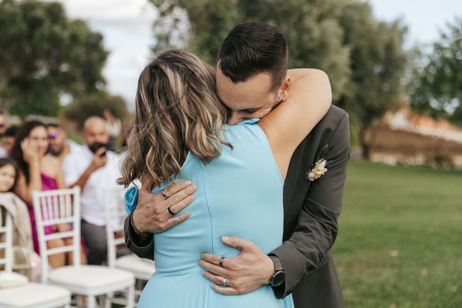 A couple share an intimate dance moment at an outdoor wedding reception with guests looking on.