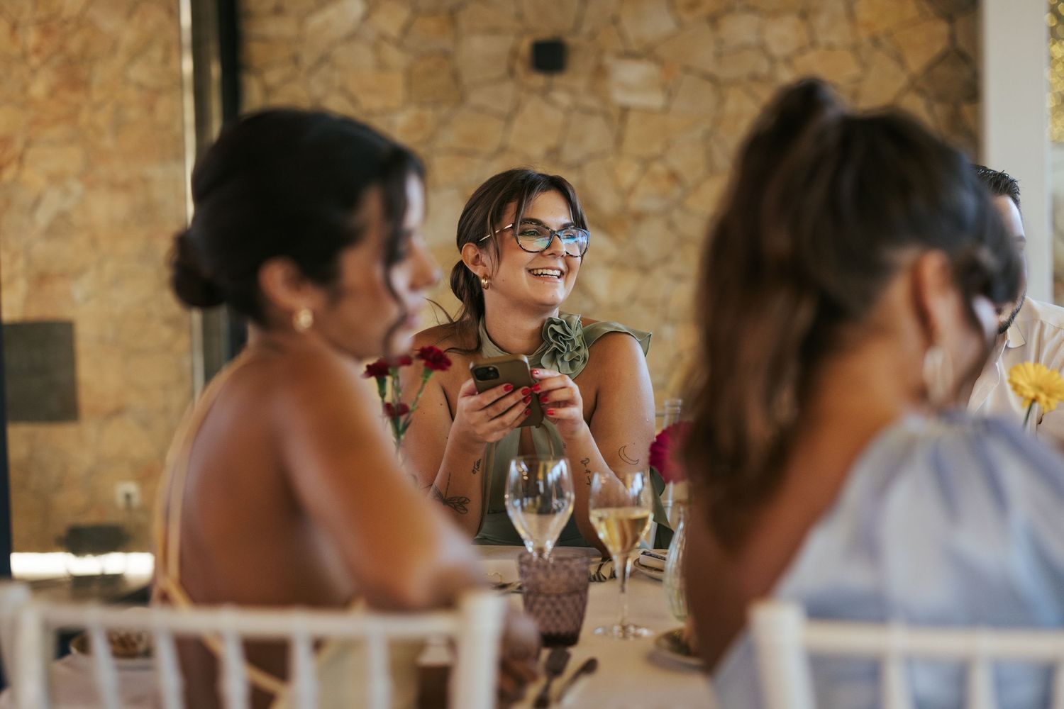 Wedding guests at a reception share a moment of laughter at their table with wine glasses.