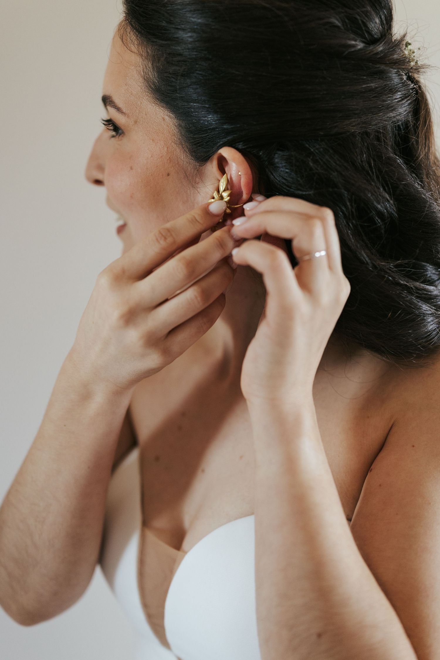 Side profile of someone putting on an earring while wearing a white strapless top.