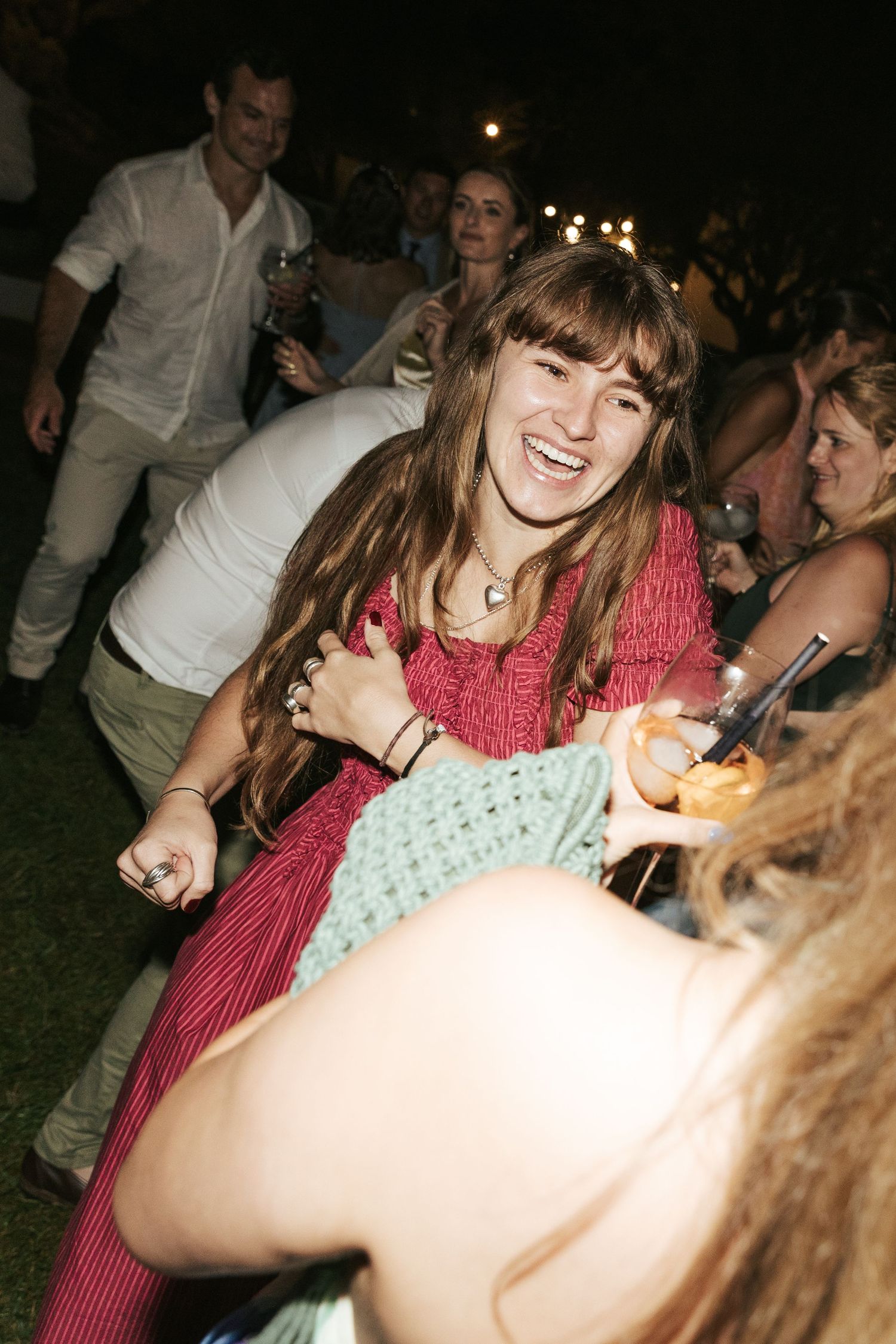 Woman in pink dress dancing and smiling at an outdoor evening event with crowd in background.