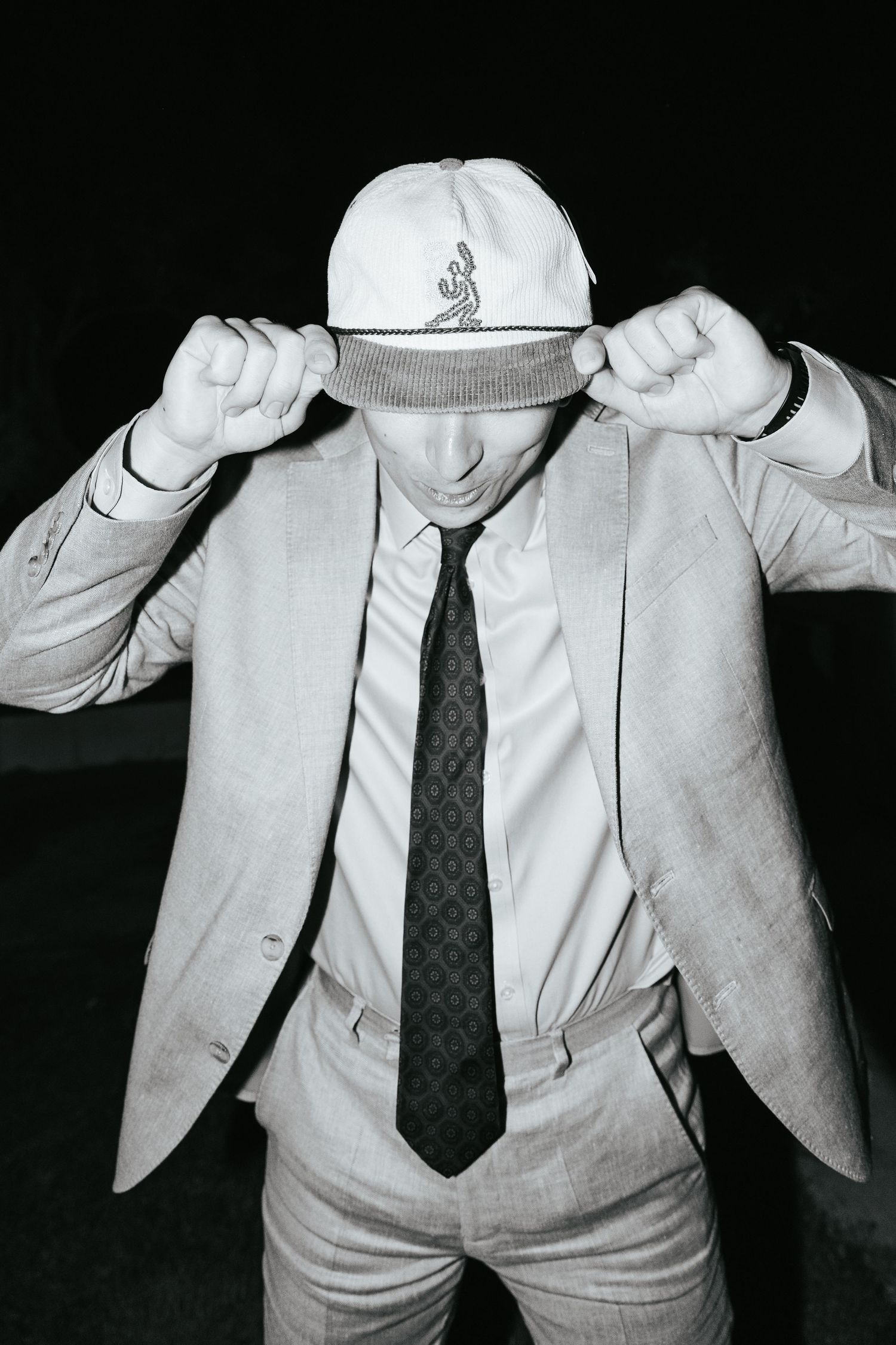 Man in suit and tie posing with a white cap at a formal evening event.