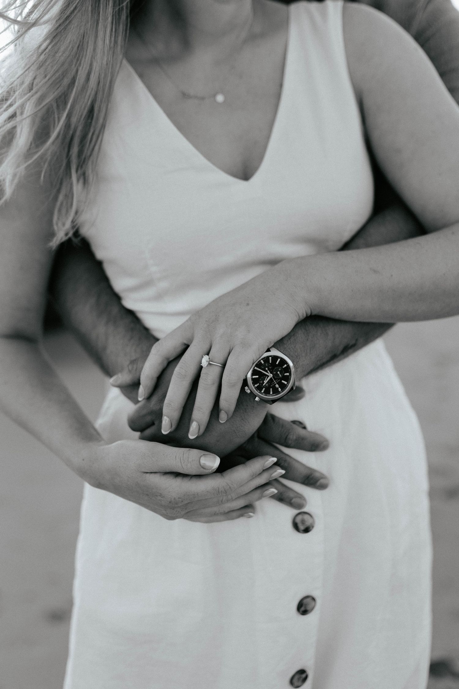 Close up of hands wearing a watch and ring against a white summery dress with buttons.