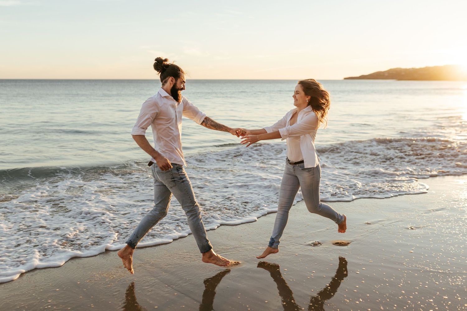 A playful couple dancing in the shallow ocean waves at sunset. Praia da Luz, Lagos, Algarve, Portugal.
