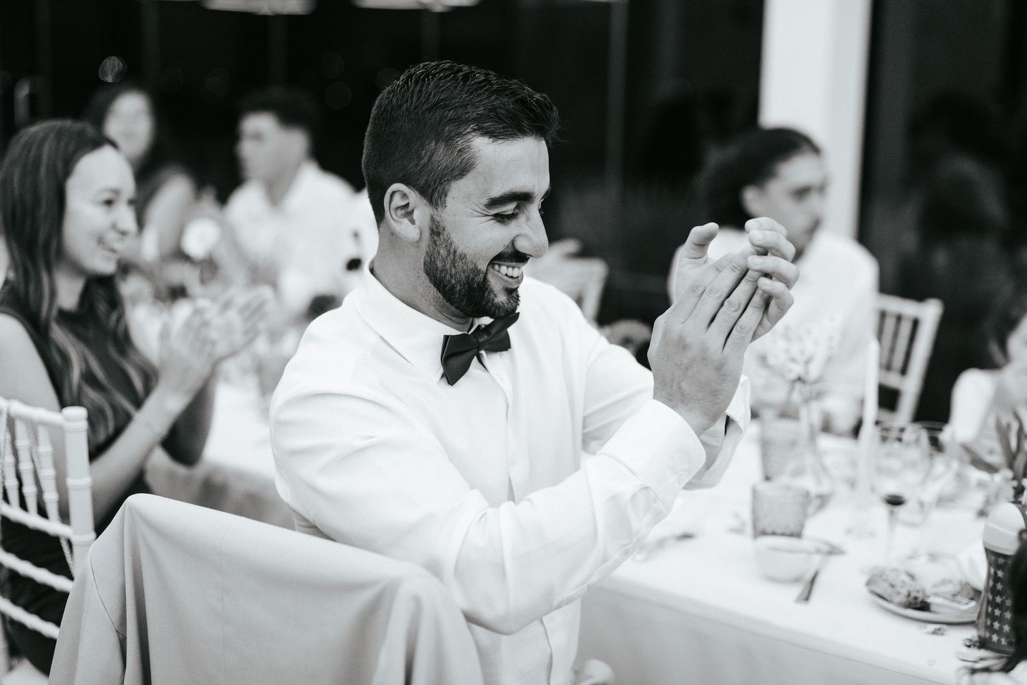 Wedding guest in white shirt and bow tie laughing joyfully during reception dinner.