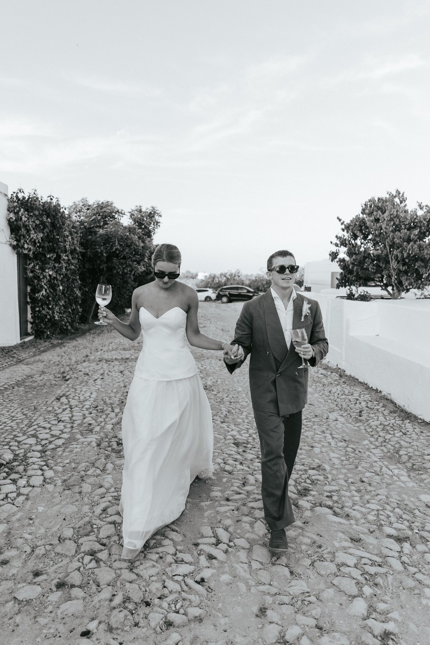 A couple walks hand in hand along a stone pathway in black and white wedding attire.