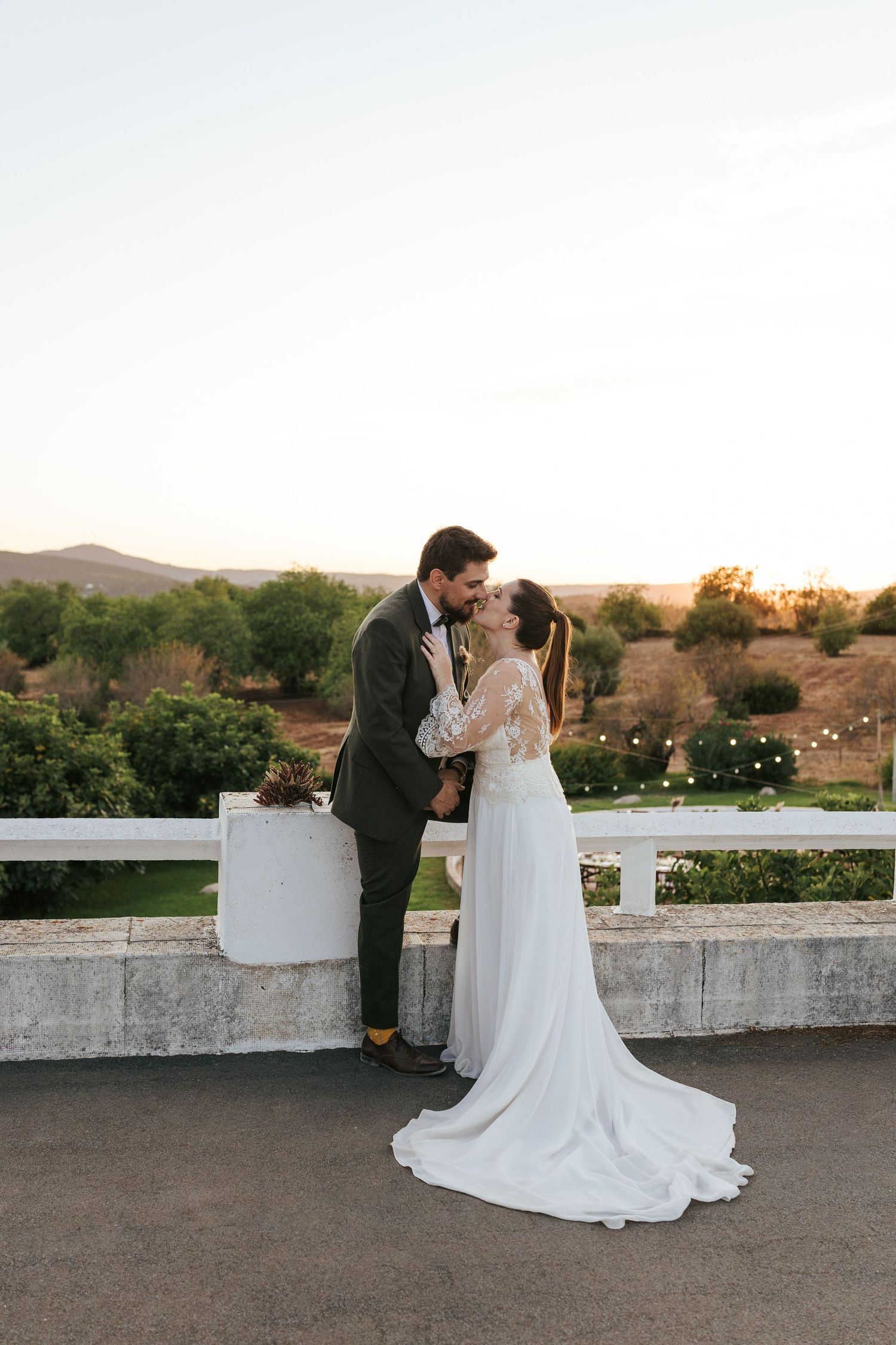 A romantic sunset wedding moment with a couple embracing on a stone balcony overlooking rolling hills.