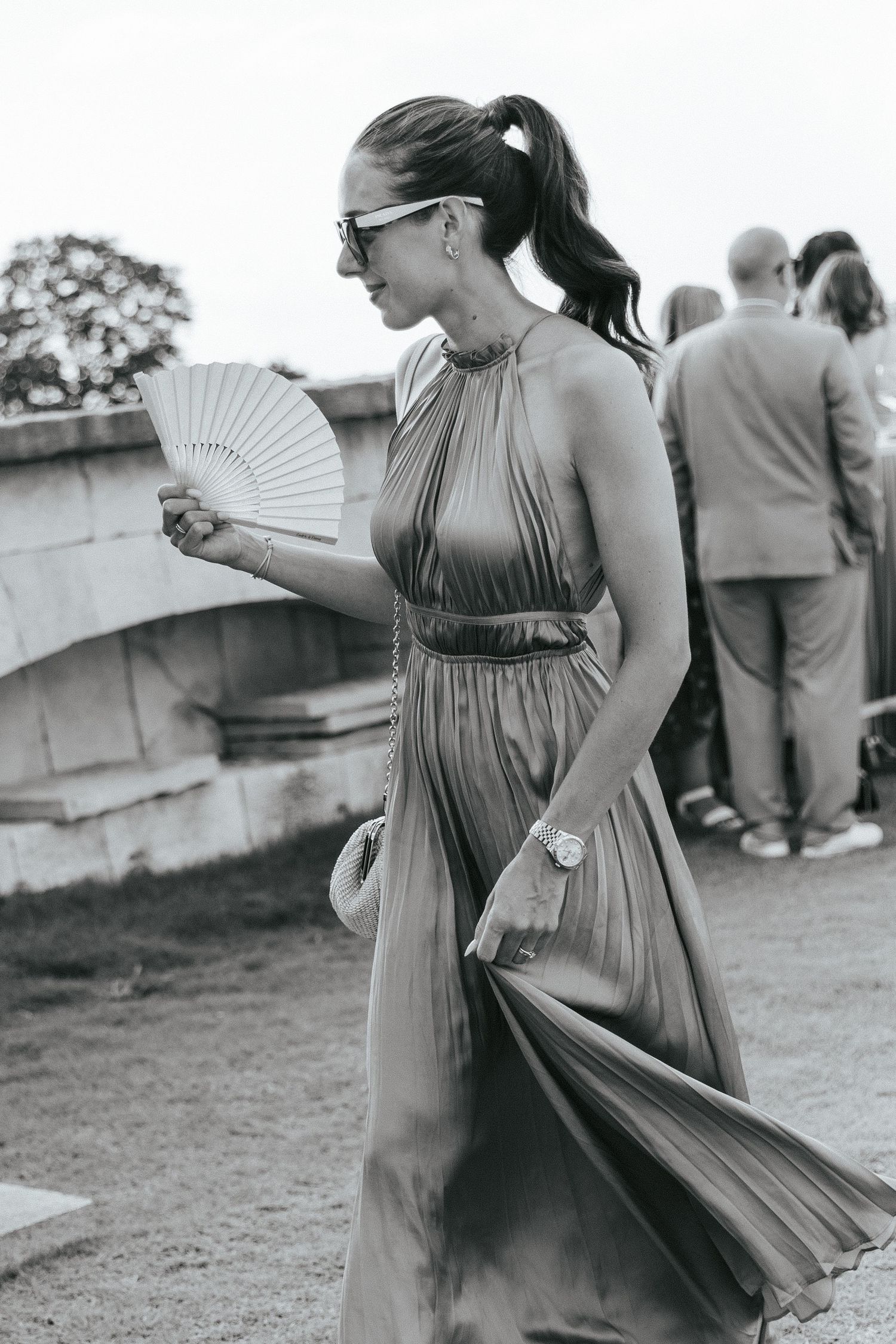 Elegant guest in flowing dress holding fan at outdoor event.