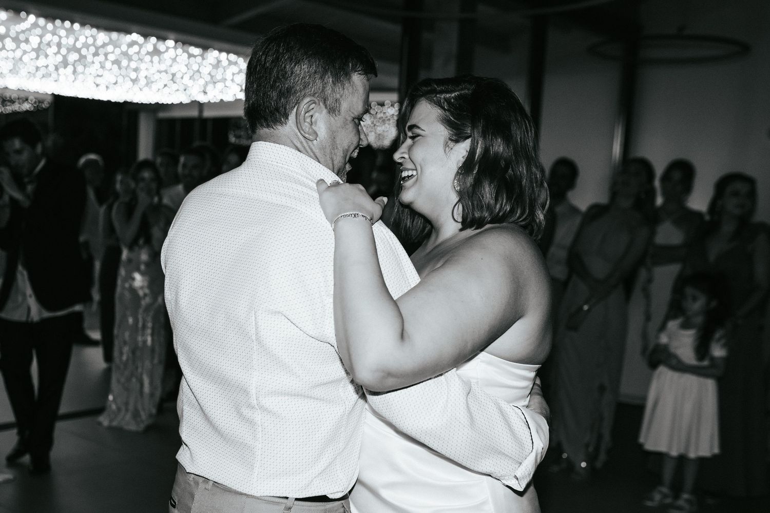 A couple shares an intimate dance moment at their wedding reception under twinkle lights in black and white photography.