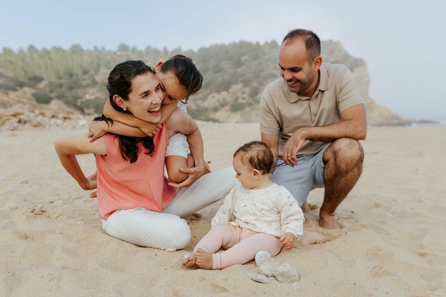 Family enjoying a casual moment together while sitting on a sandy beach on a sunny day.