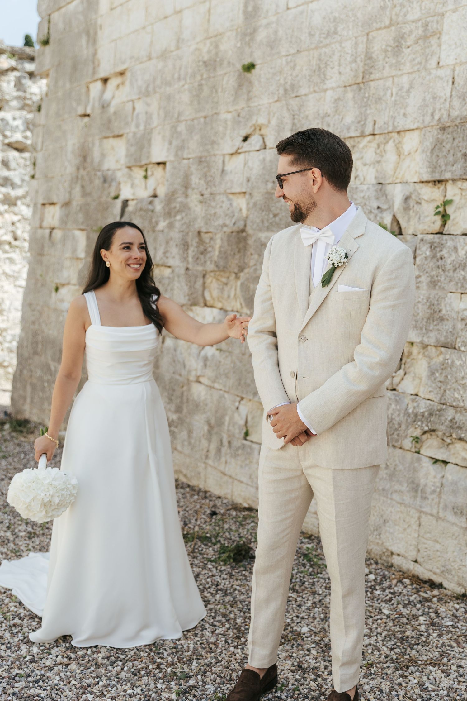 A couple in wedding attire shares intimate moments against a rustic stone wall backdrop.
