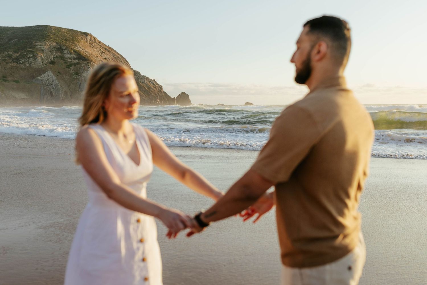 A couple shares a romantic moment on a misty beach shoreline at golden hour.