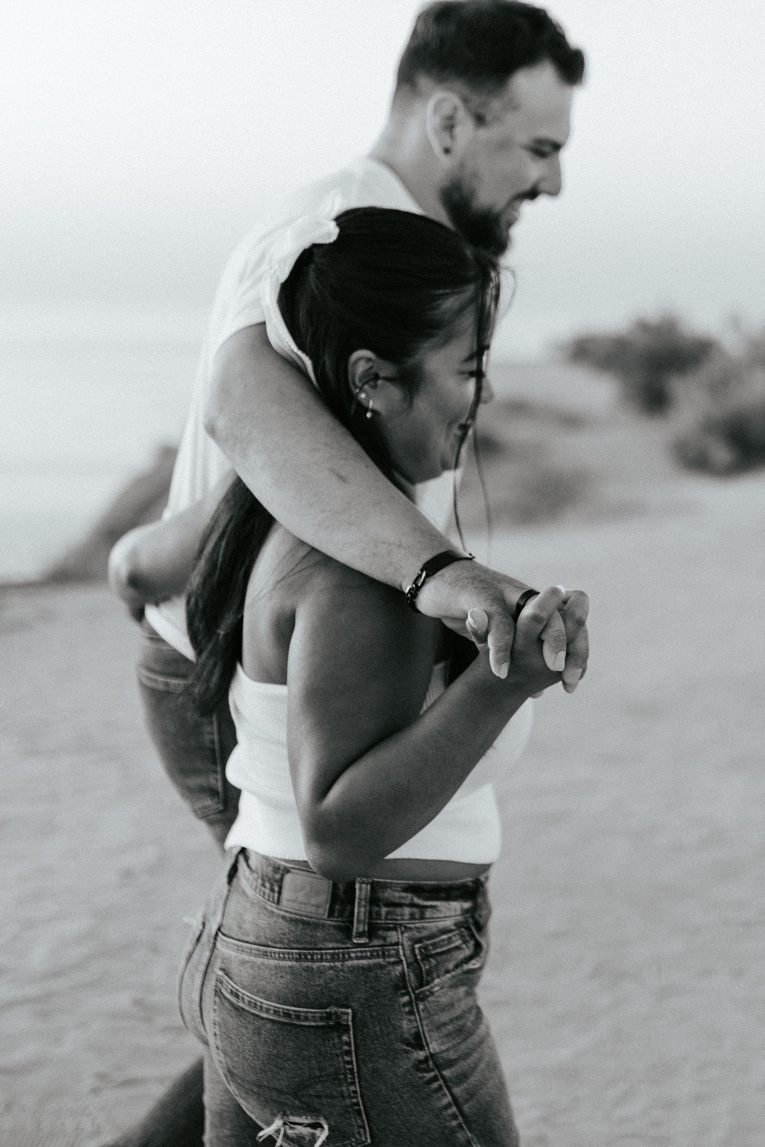 A romantic black and white photo shows a couple embracing on a beach, captured in an intimate candid moment.