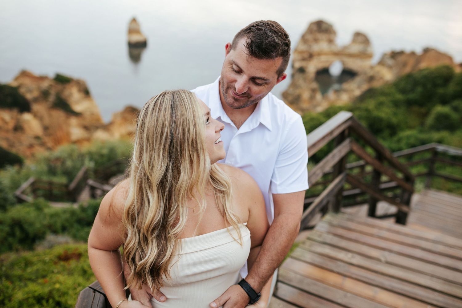 Intimate embrace on wooden deck overlooking rocky coastline and sea. Praia do Camilo, Lagos, Algarve, Portugal.
