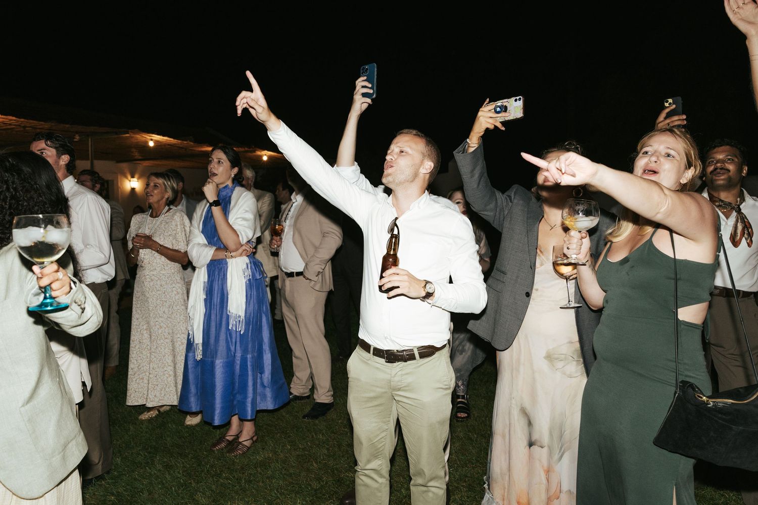 Guests dancing and taking photos at an outdoor evening wedding reception celebration.