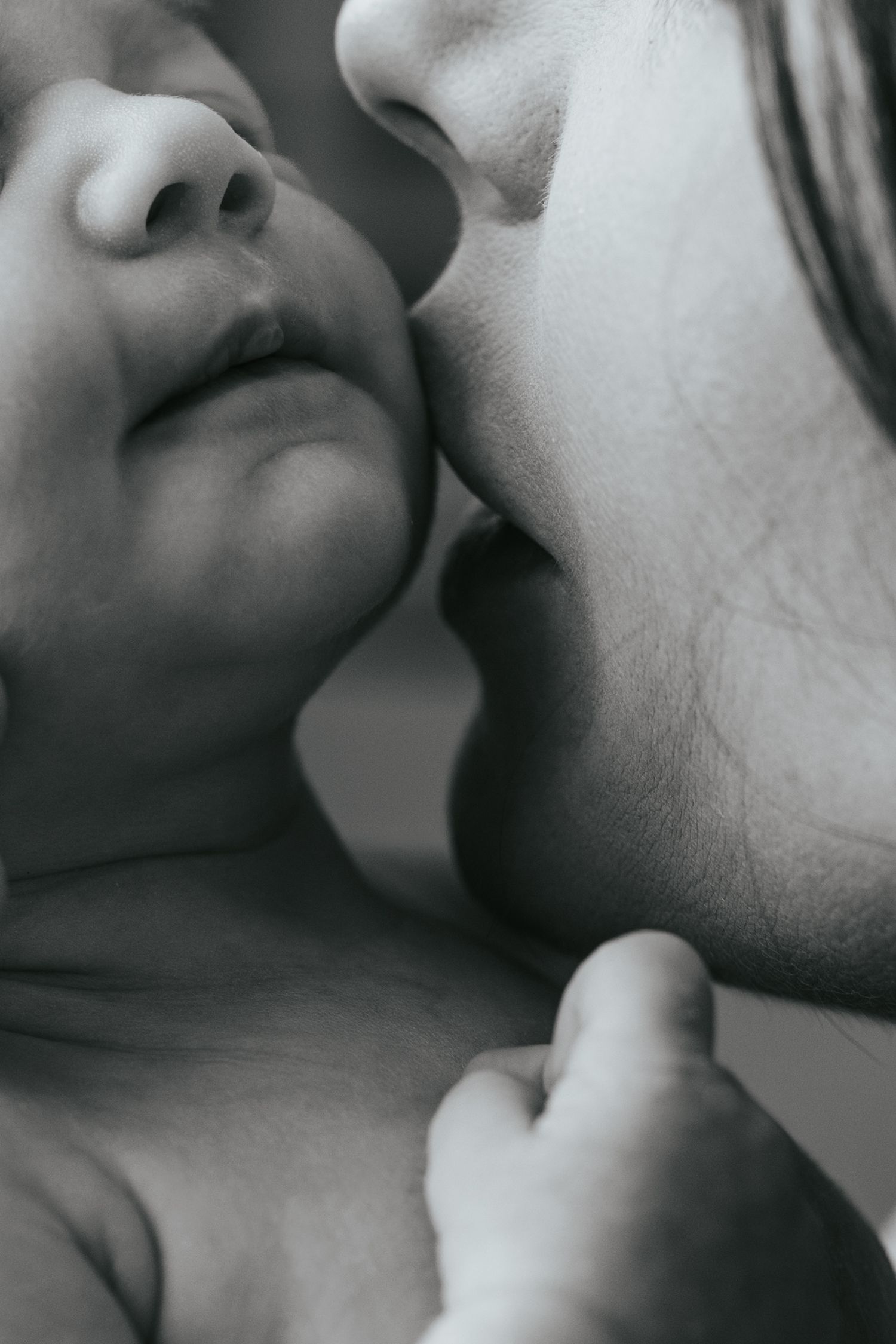 Black and white close-up photo of a mother tenderly kissing her newborn baby's cheek.