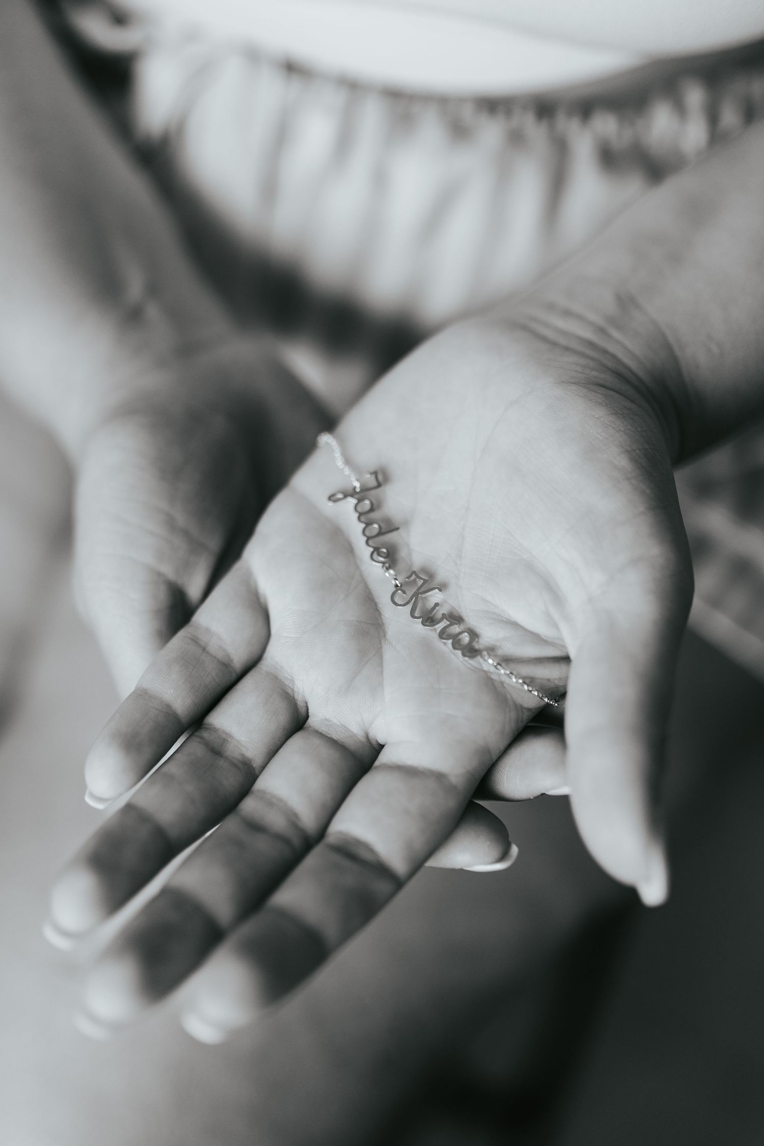 Black and white close-up of a hand displaying a delicate bracelet with cursive text.