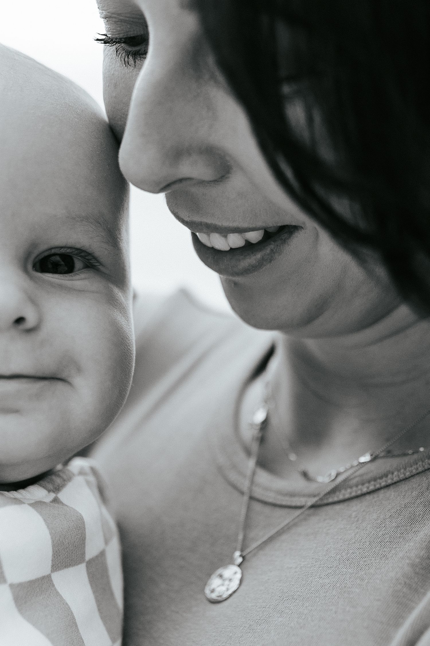 A close-up black and white portrait capturing a tender intimate moment between a baby and parent.
