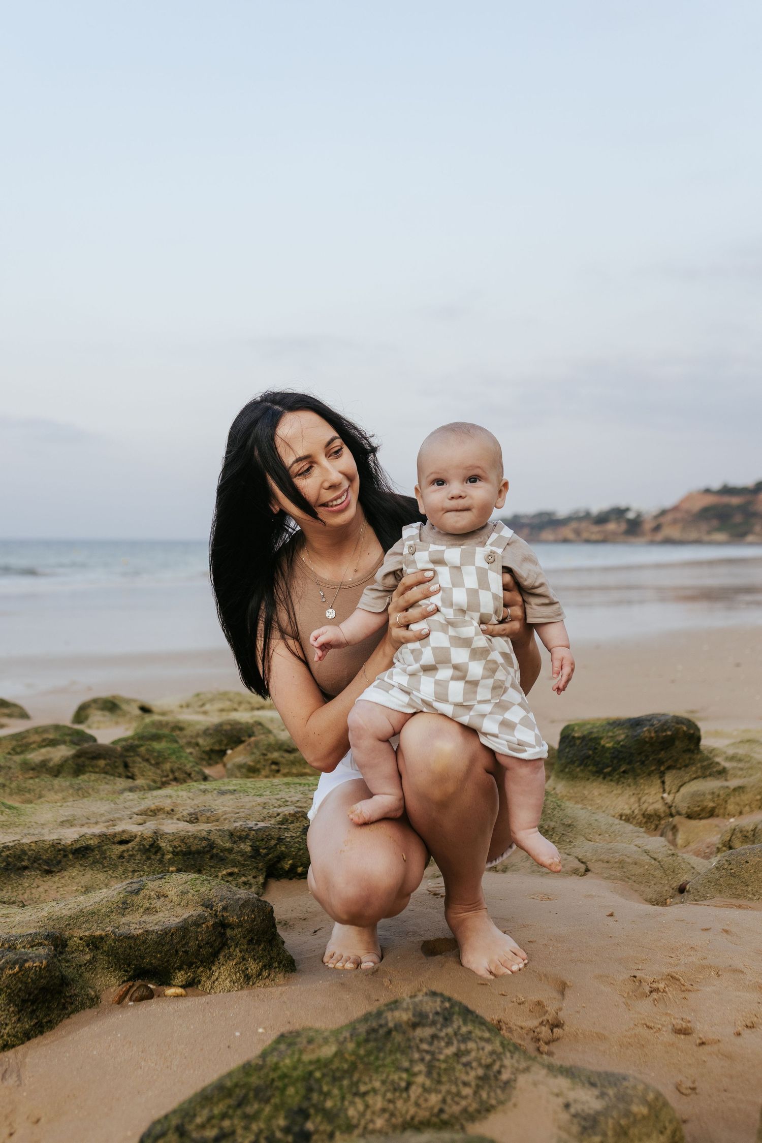 A joyful moment captured on a rocky beach as they pose together near the ocean on a cloudy day.