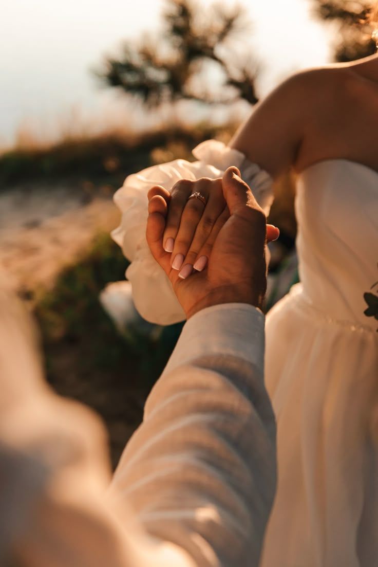 Two hands tenderly clasped together in warm sunset lighting, creating an intimate and romantic moment outdoors.
