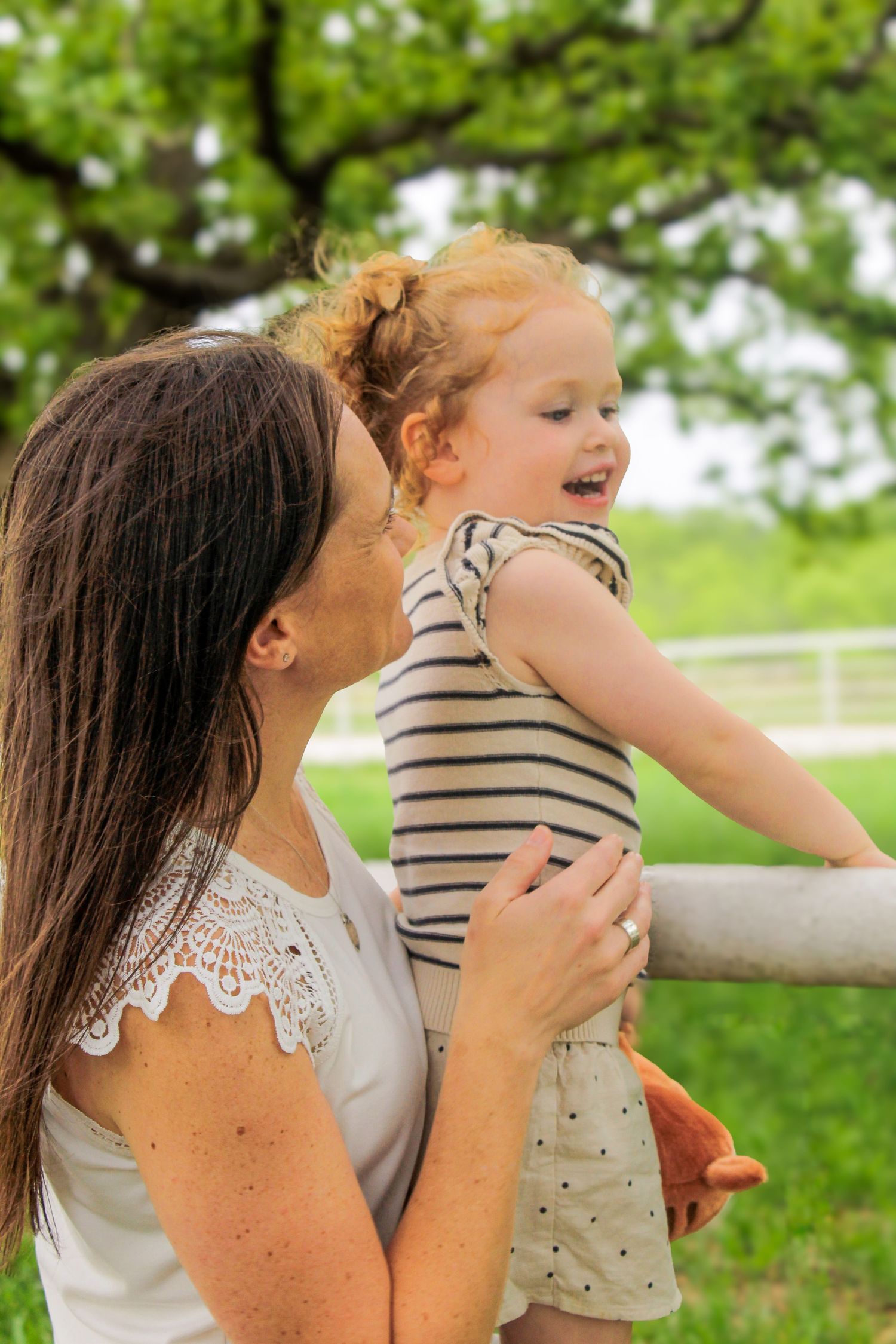 A joyful outdoor moment with a child in striped outfit being lifted up against a green background.