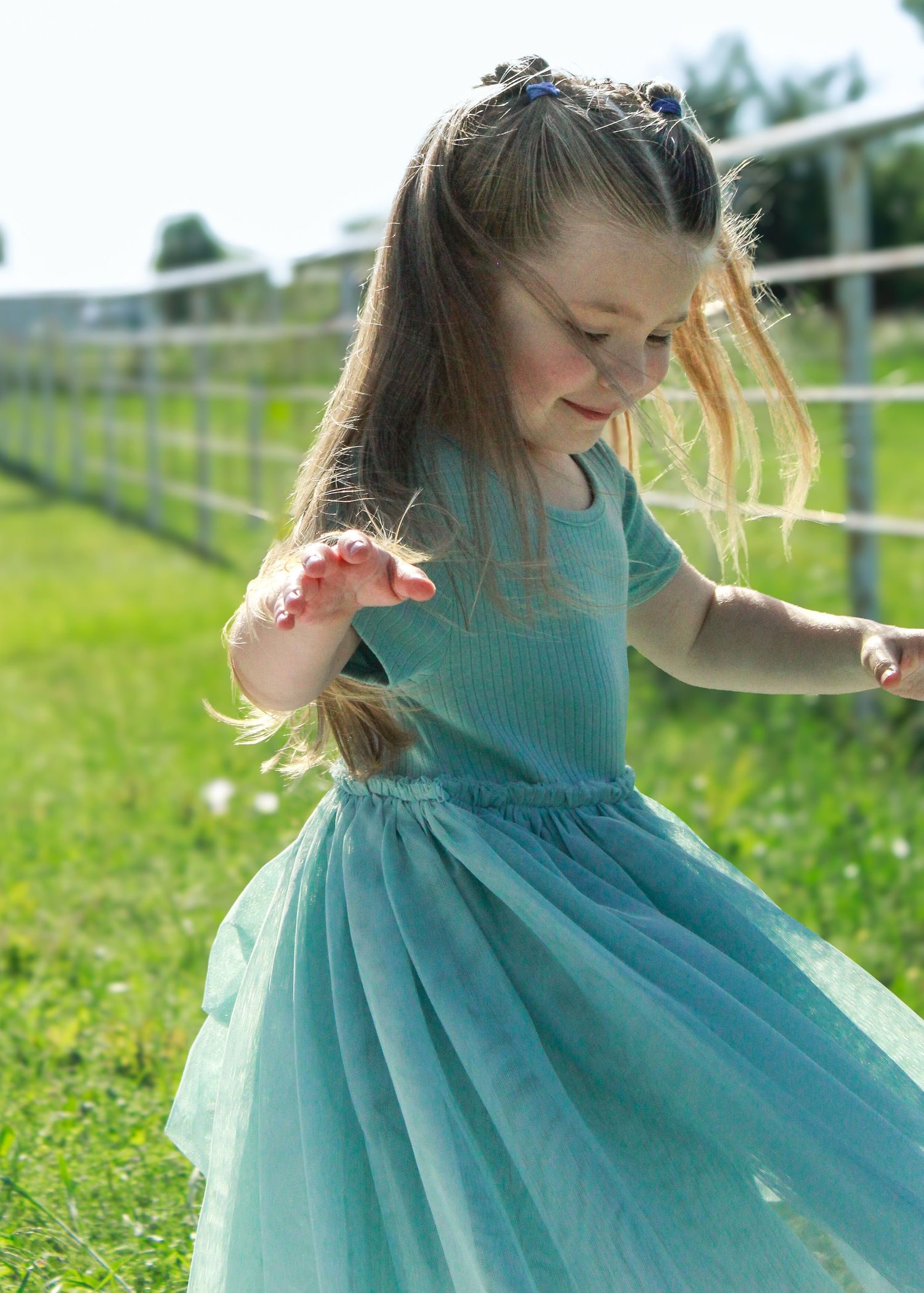 Child in flowing turquoise dress twirling in a sunny field with white flowers.