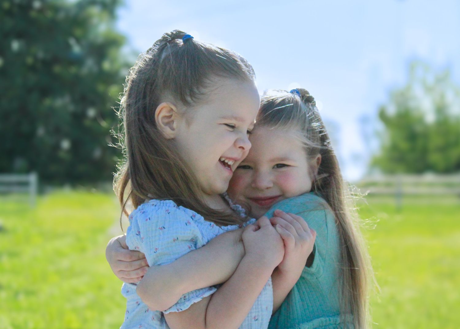 Children hugging each other outdoors in a green summer setting.