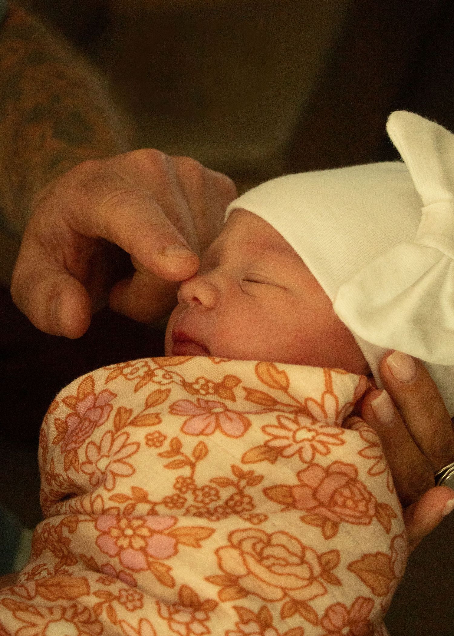 A tiny baby is peacefully sleeping swaddled in a floral patterned blanket with orange and pink flowers.